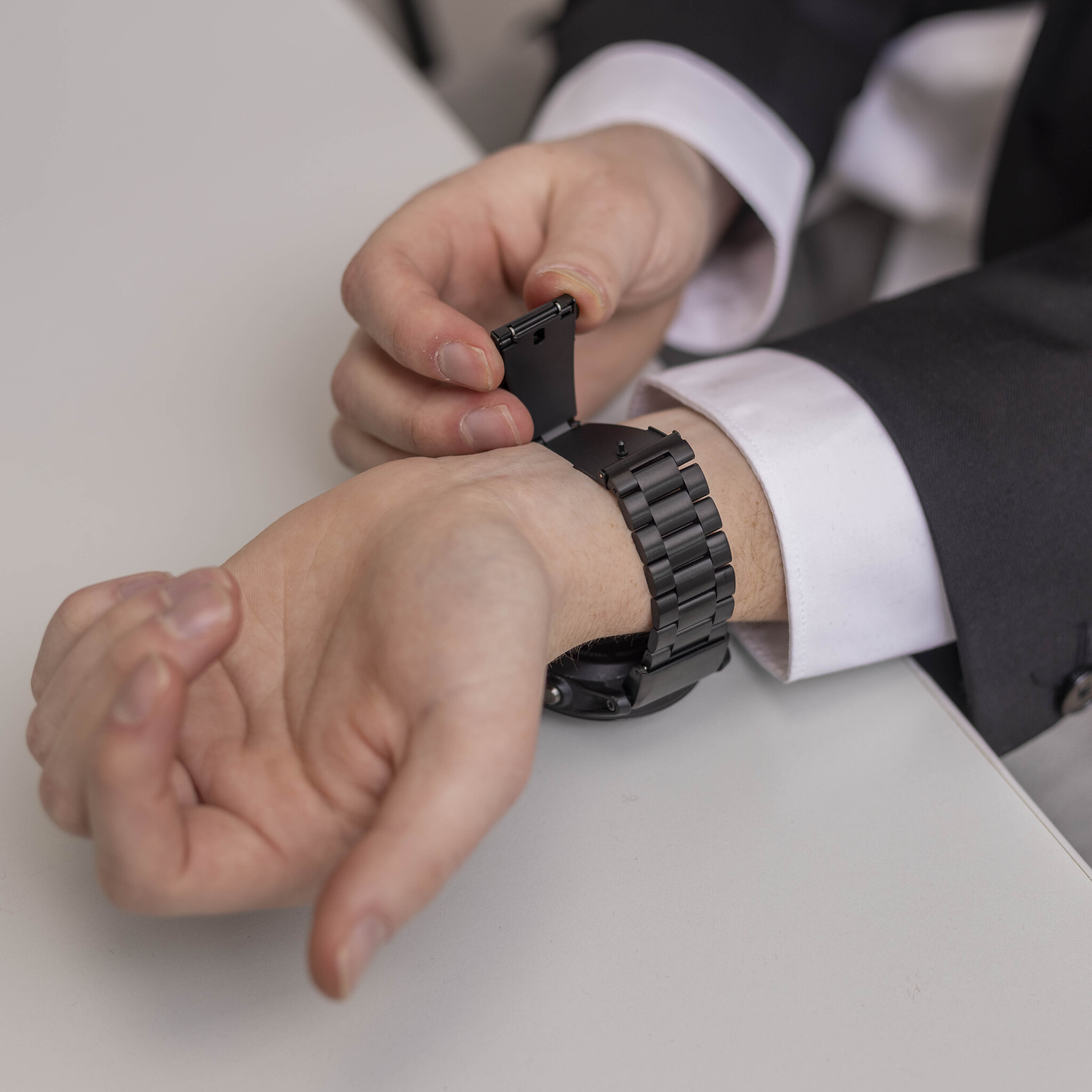 Männerhände, die eine schwarze Metalluhr einstellen. Die Uhr hat ein schwarzes Armband, und der Hintergrund ist hell.