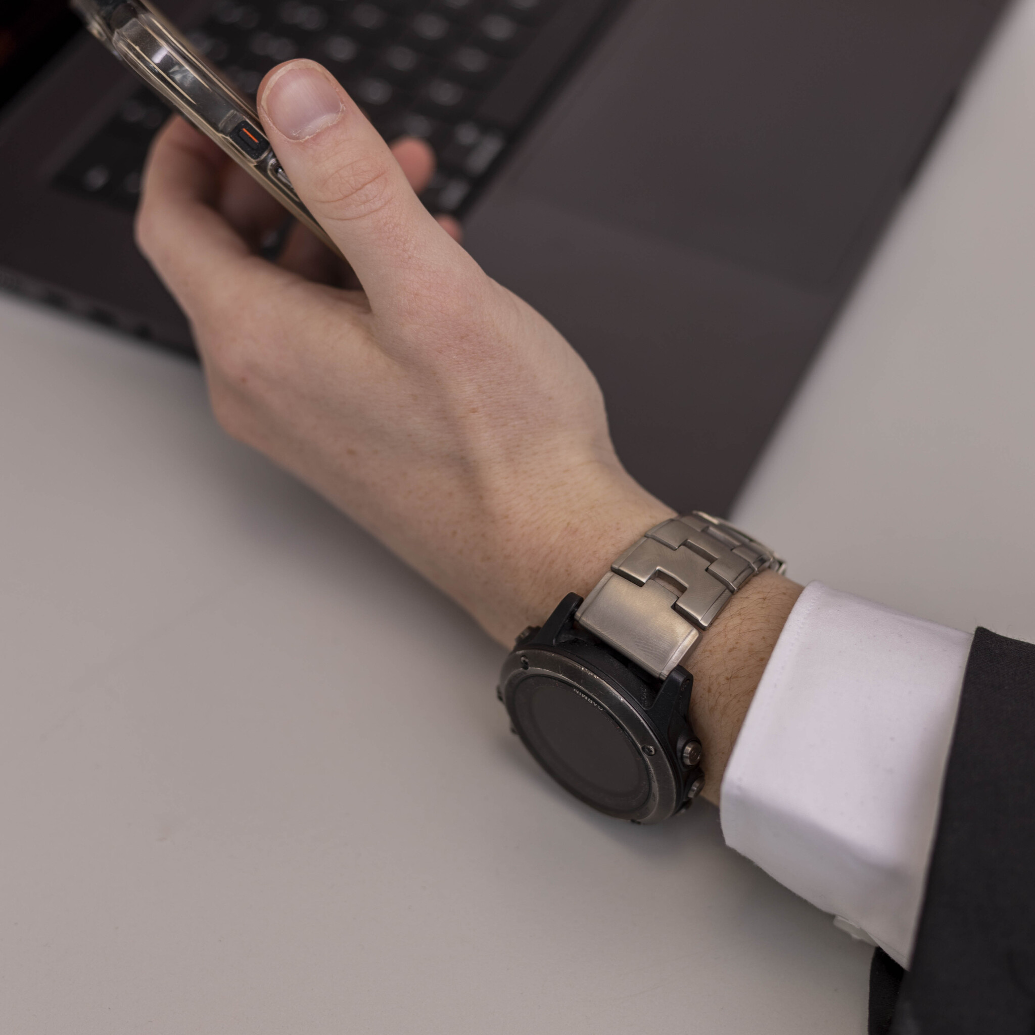 Ein Arm mit Uhr und Telefon. Die Person trägt einen Anzug.