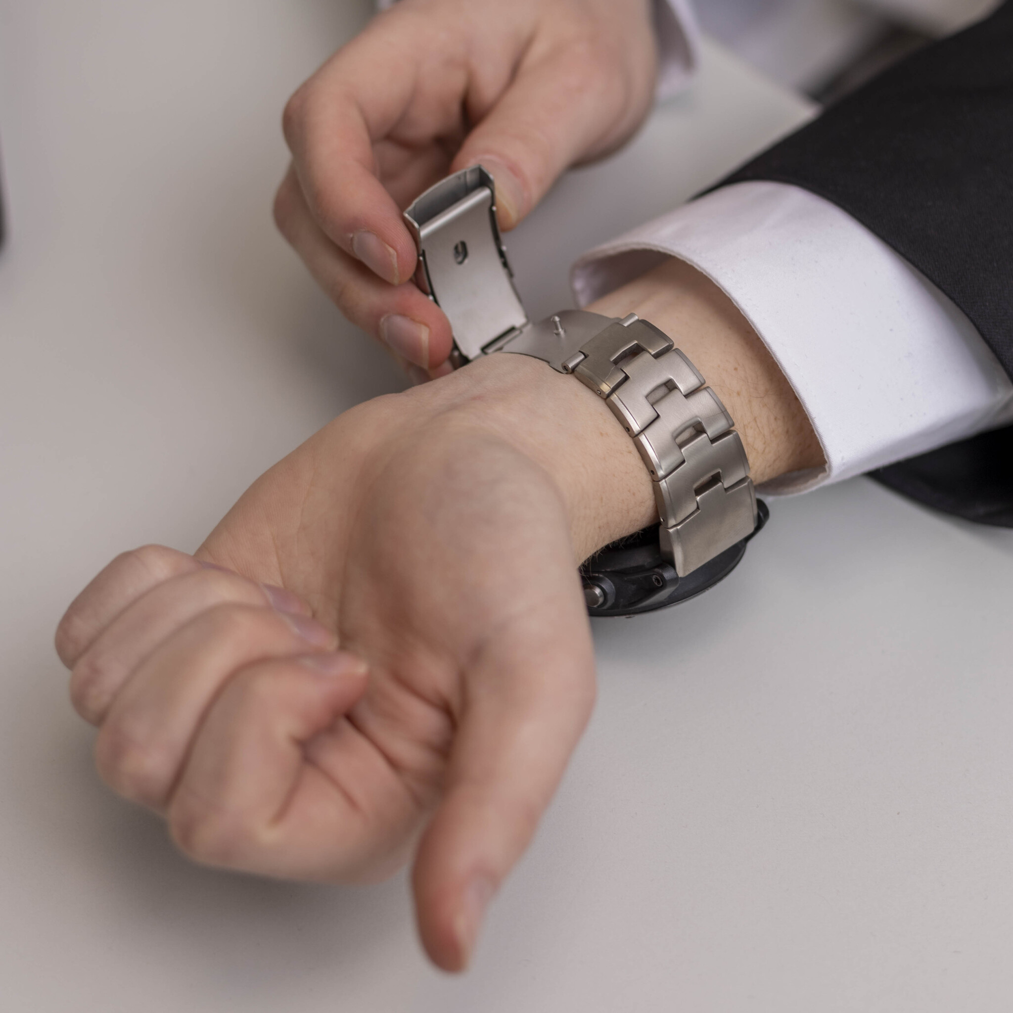 Jemand justiert eine silberne Uhr an ihrem Handgelenk. Die Uhr ist metallisch, der Hintergrund ist weiß.