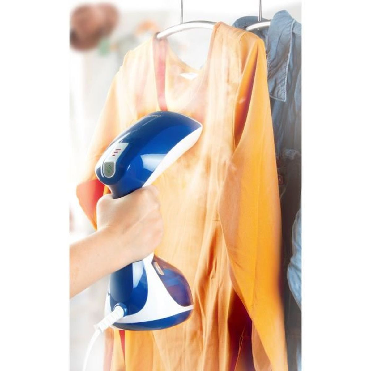 Eine Hand hält einen blau-weißen Dampfgarer, der ein orangefarbenes Kleid auf einem Bügel dampft.