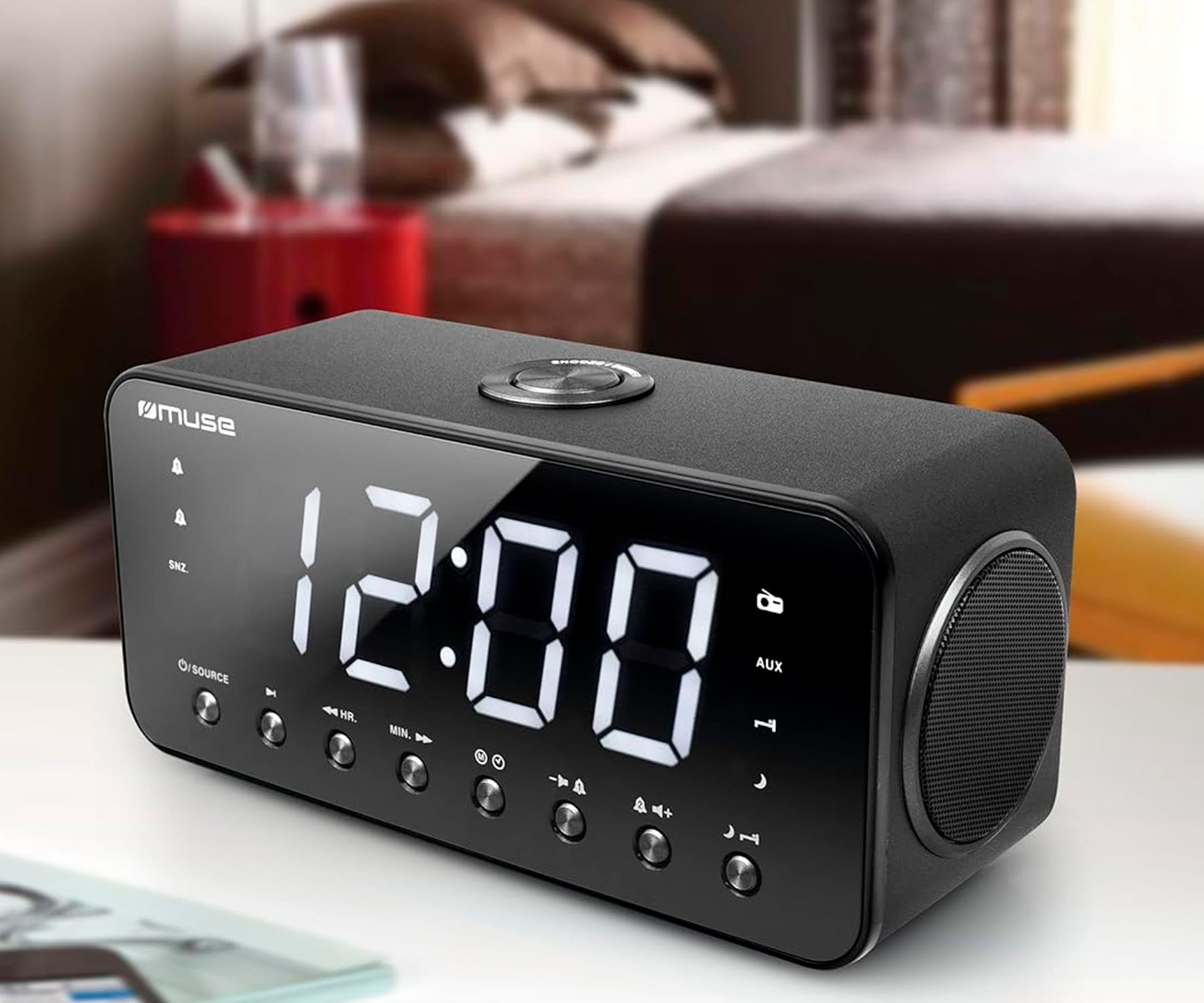 Czarny budzik cyfrowy z godziną 12:00. Na białym stole. Rozmyte tło sypialni.