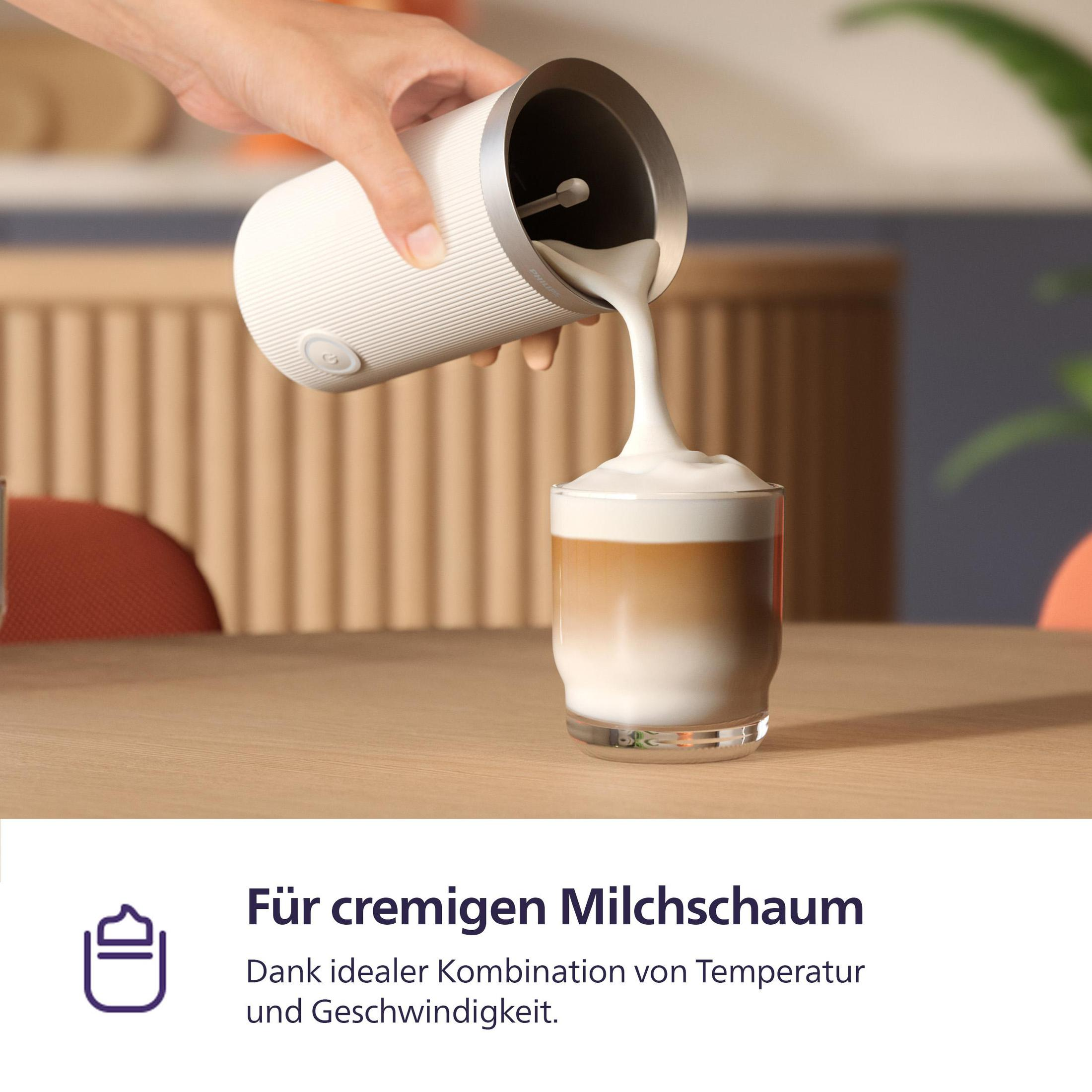 Eine Hand gießt Milchschaum aus einem weißen Aufschäumer in ein Glas geschichteten Kaffees.