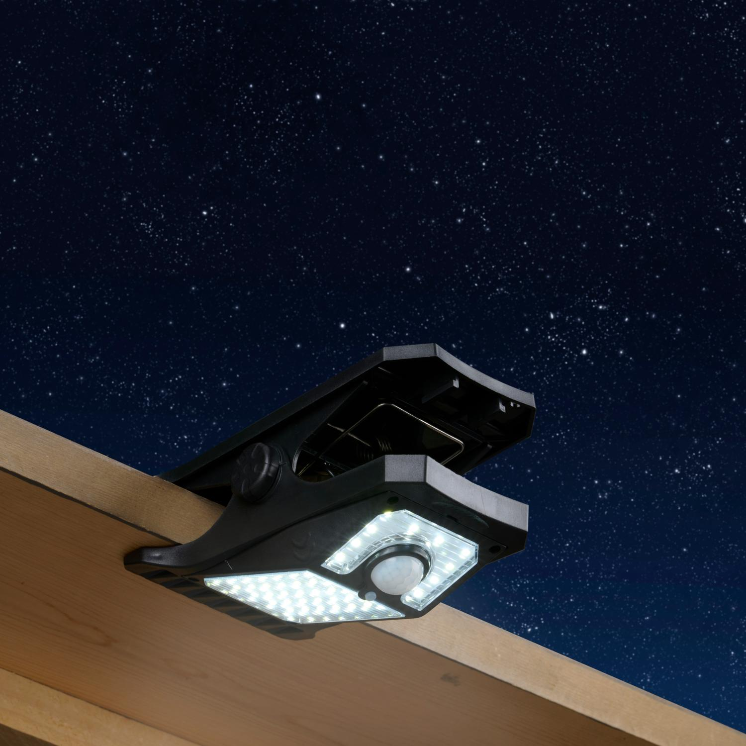 Zonne-aangedreven buitenlamp met een klem, gemonteerd op hout, tegen een sterrenhemel.
