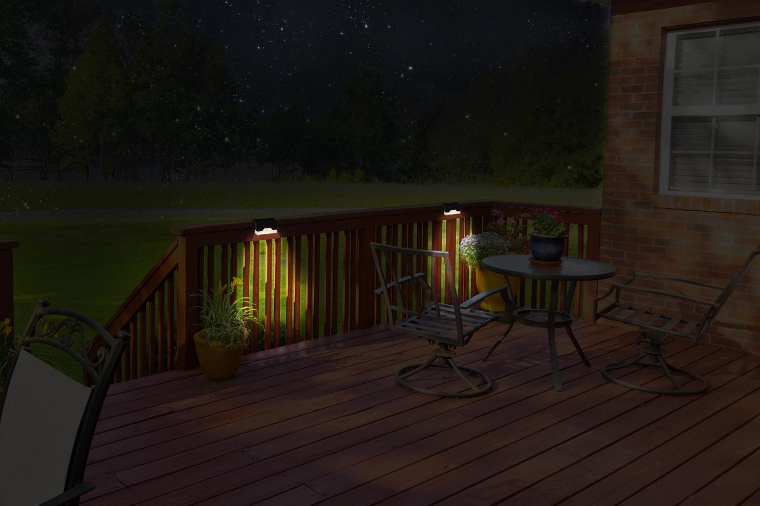 Night scene with lit deck lights, table, chairs, and plants. Background shows a green lawn and night sky.