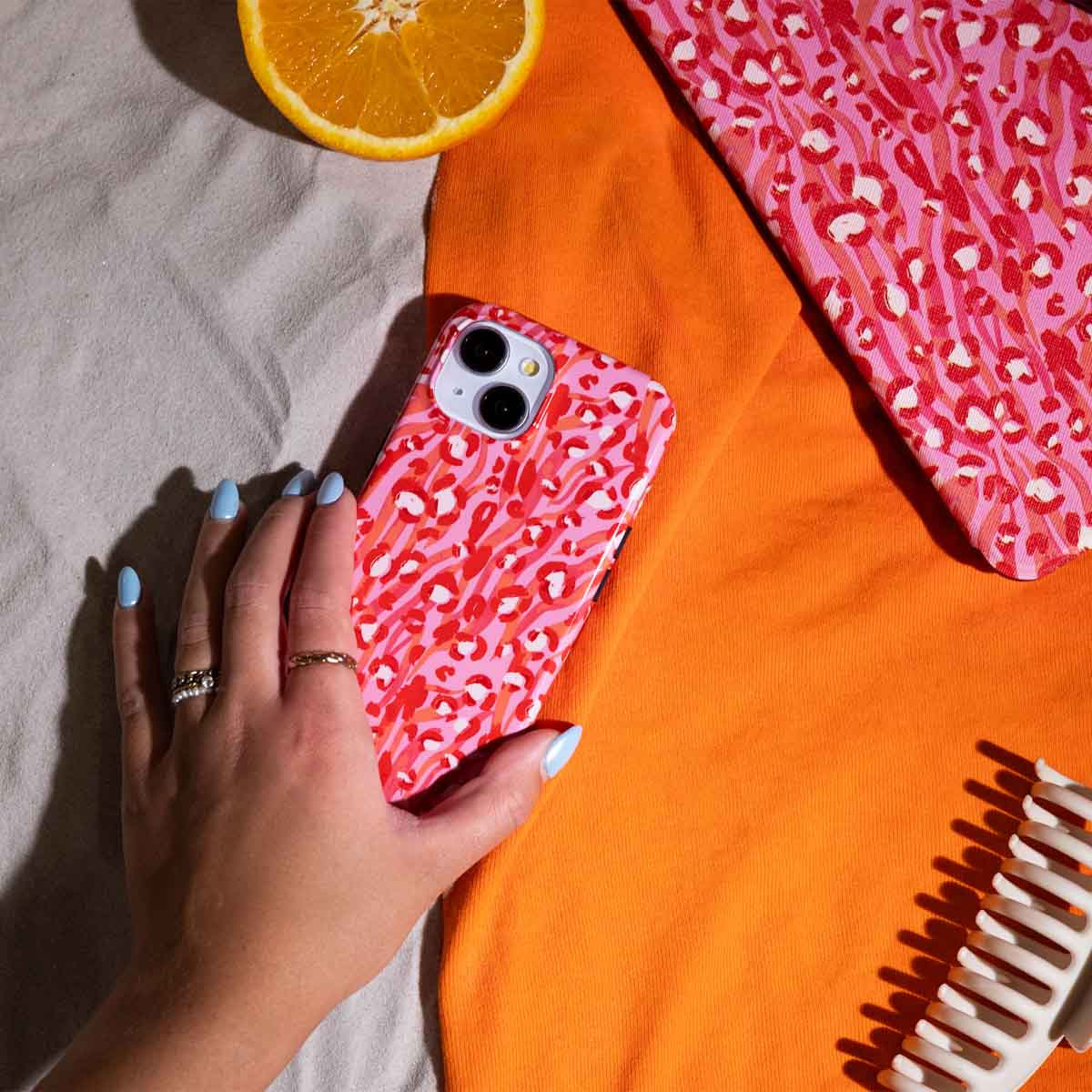 Vrouw hand met roze luipaard print telefoonhoesje. Oranje achtergrond, sinaasappelschijfje, roze stof, kam.