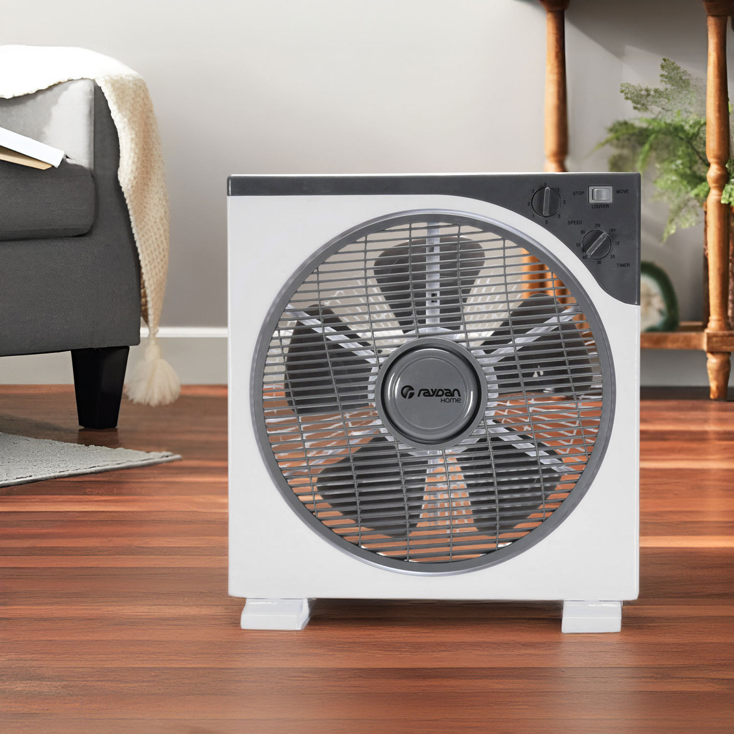 Ventilador blanco y gris sobre suelo de madera, con sillón gris.