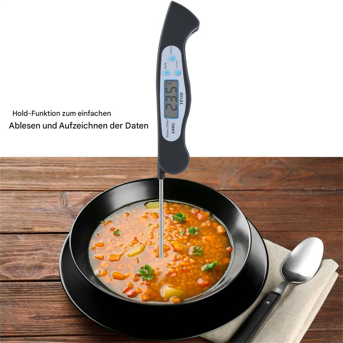 Schwarzes und blaues Lebensmittell-Thermometer misst Suppe. Schwarze Schüssel, Löffel, Holztisch.