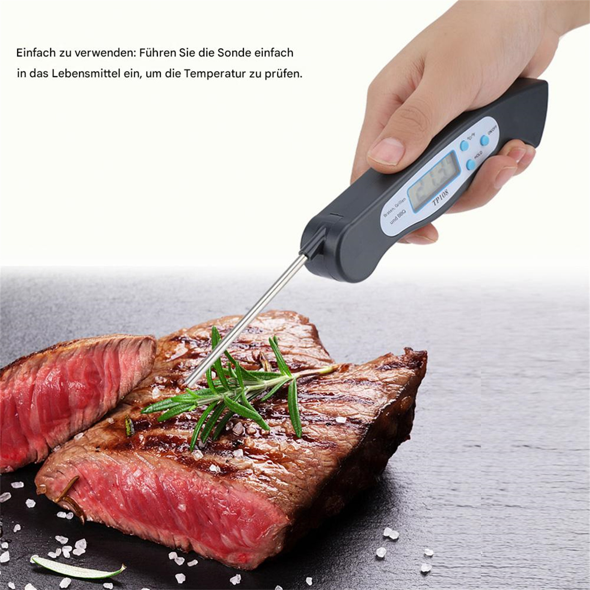 Hand hält digitales Thermometer, Fleisch und Rosmarin auf schwarzer Oberfläche.