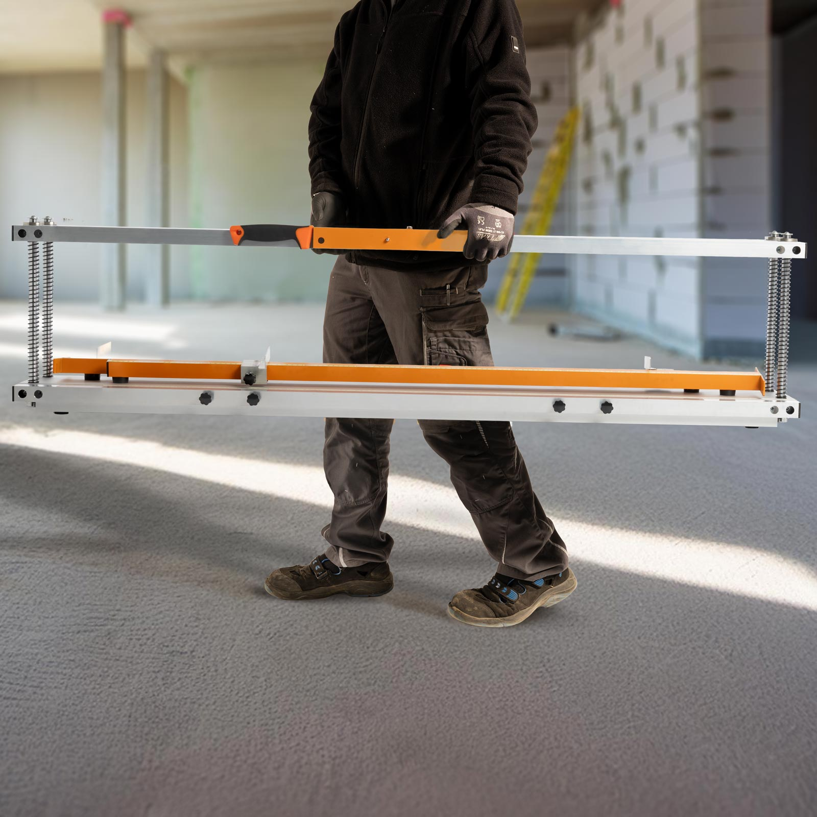 Eine Person, die ein Aluminiumwerkzeug mit orangefarbenem Griff trägt. Die Szene ist eine Baustelle.