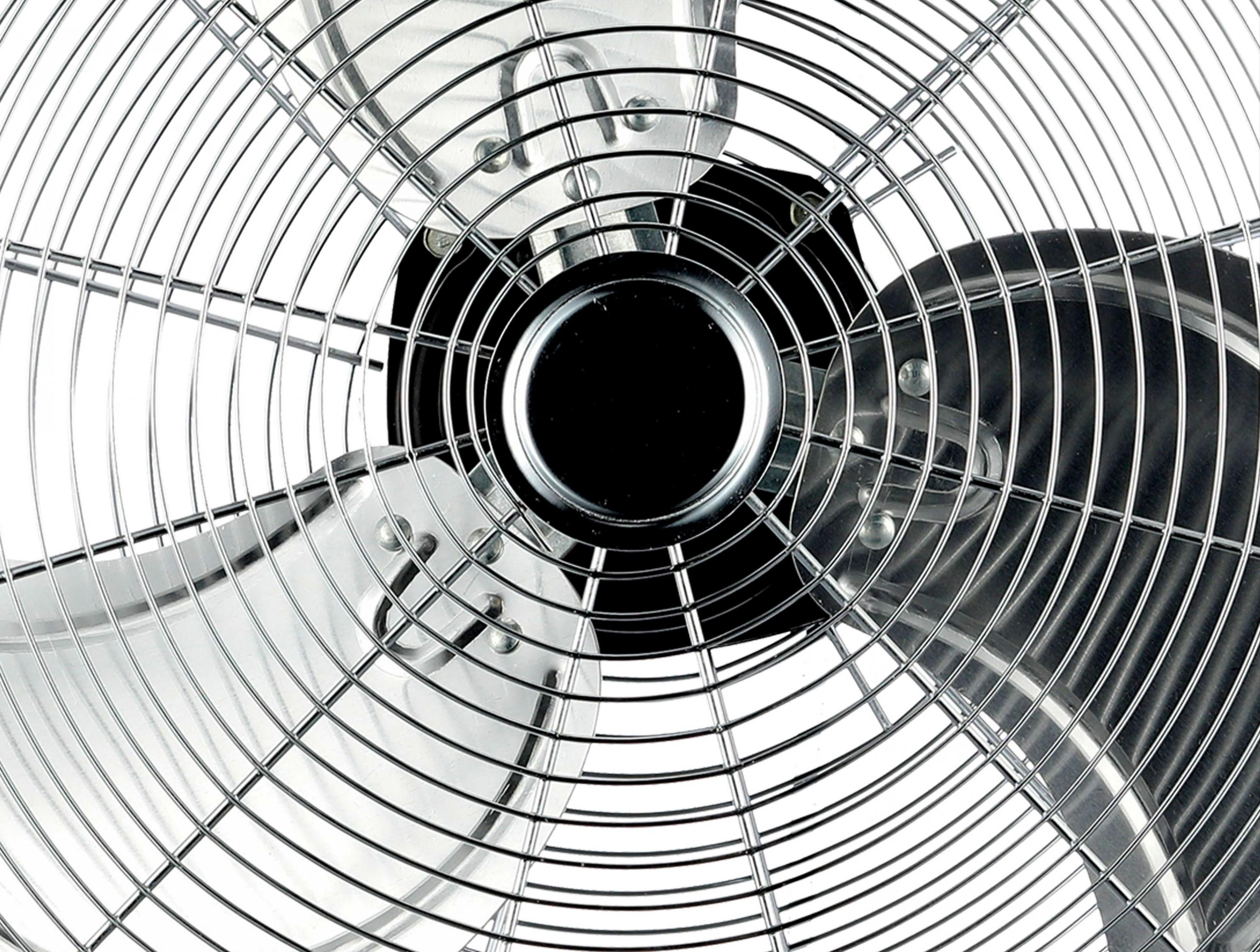 Primer plano de un ventilador metálico con una rejilla protectora. Fondo blanco.