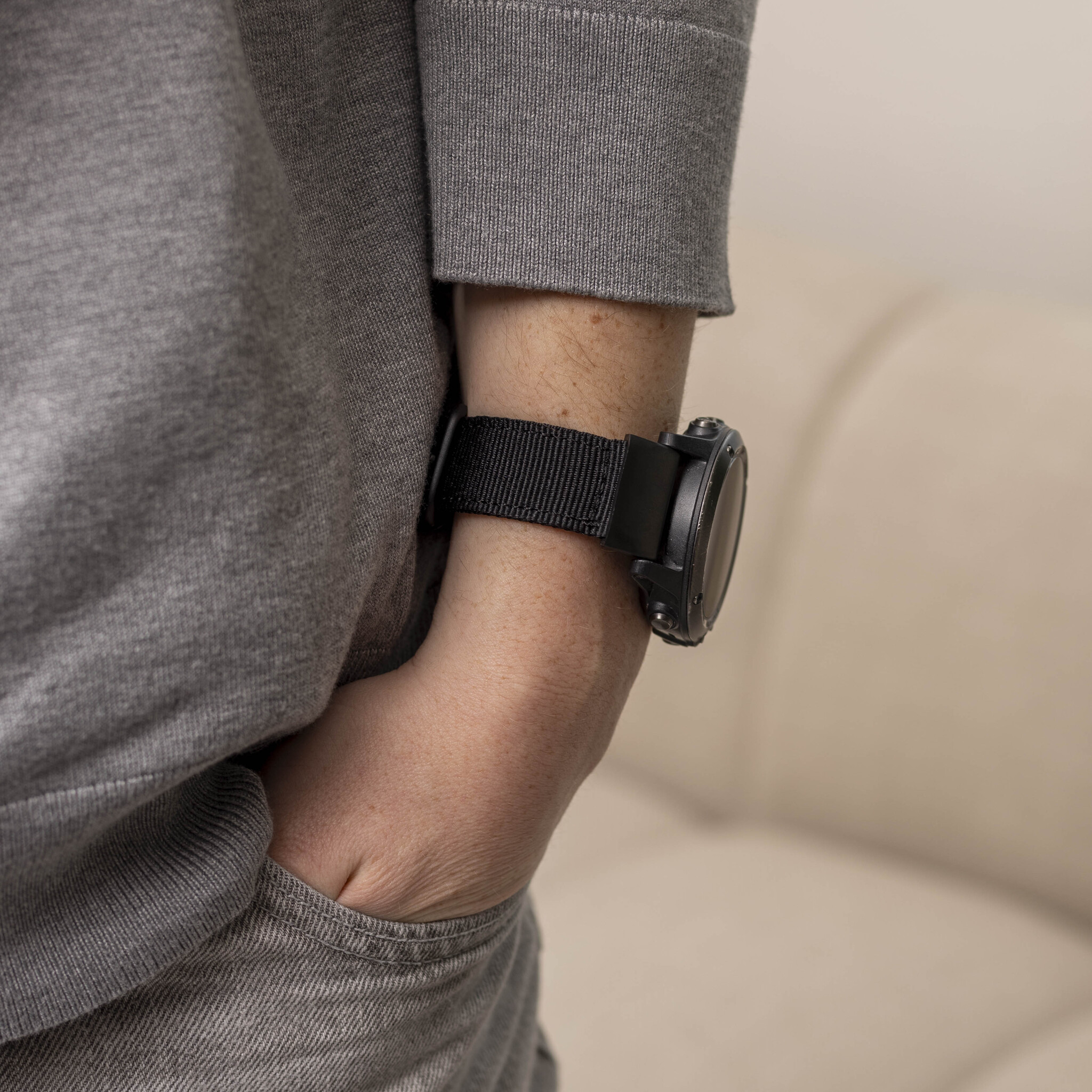 Person trägt grauen Sweatshirt, schwarze Uhr am Handgelenk, Hand in der Tasche.