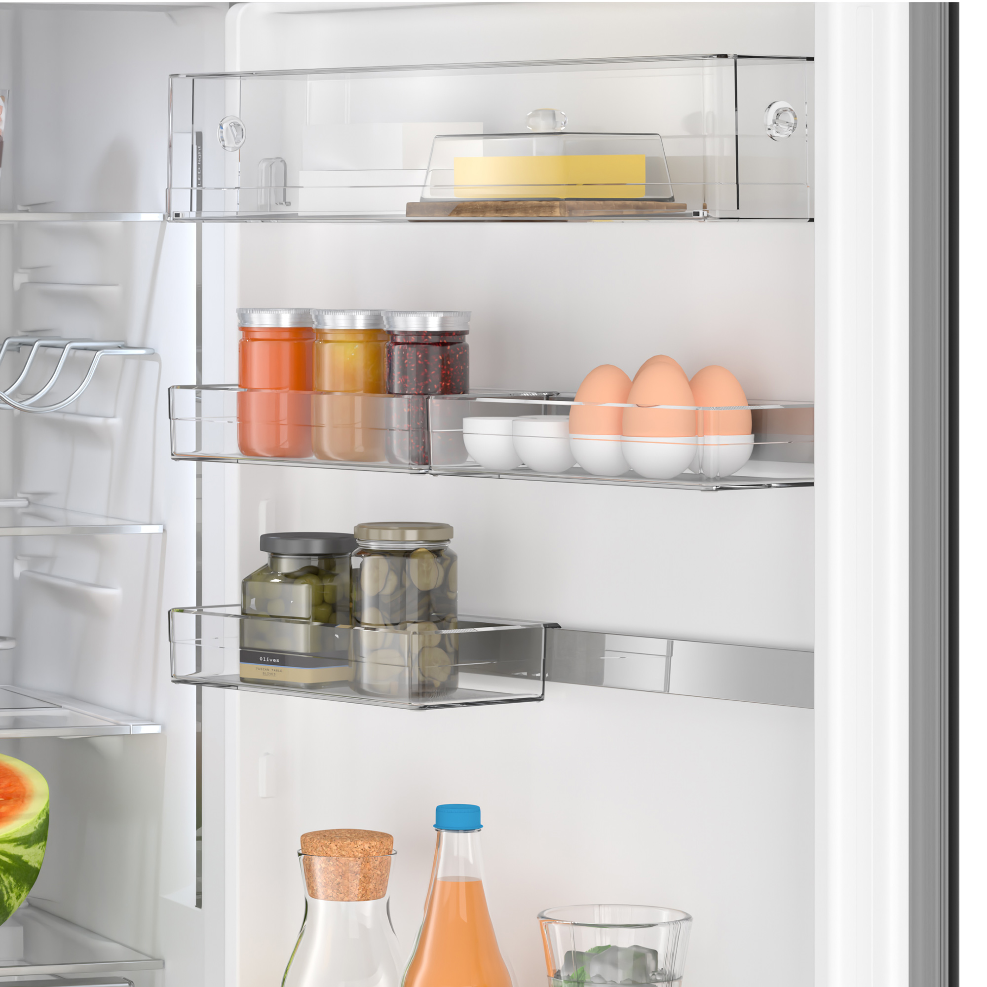 Wnętrze lodówki z półkami z słoikami, jajkami i innymi produktami spożywczymi. Arbuzy w tle.