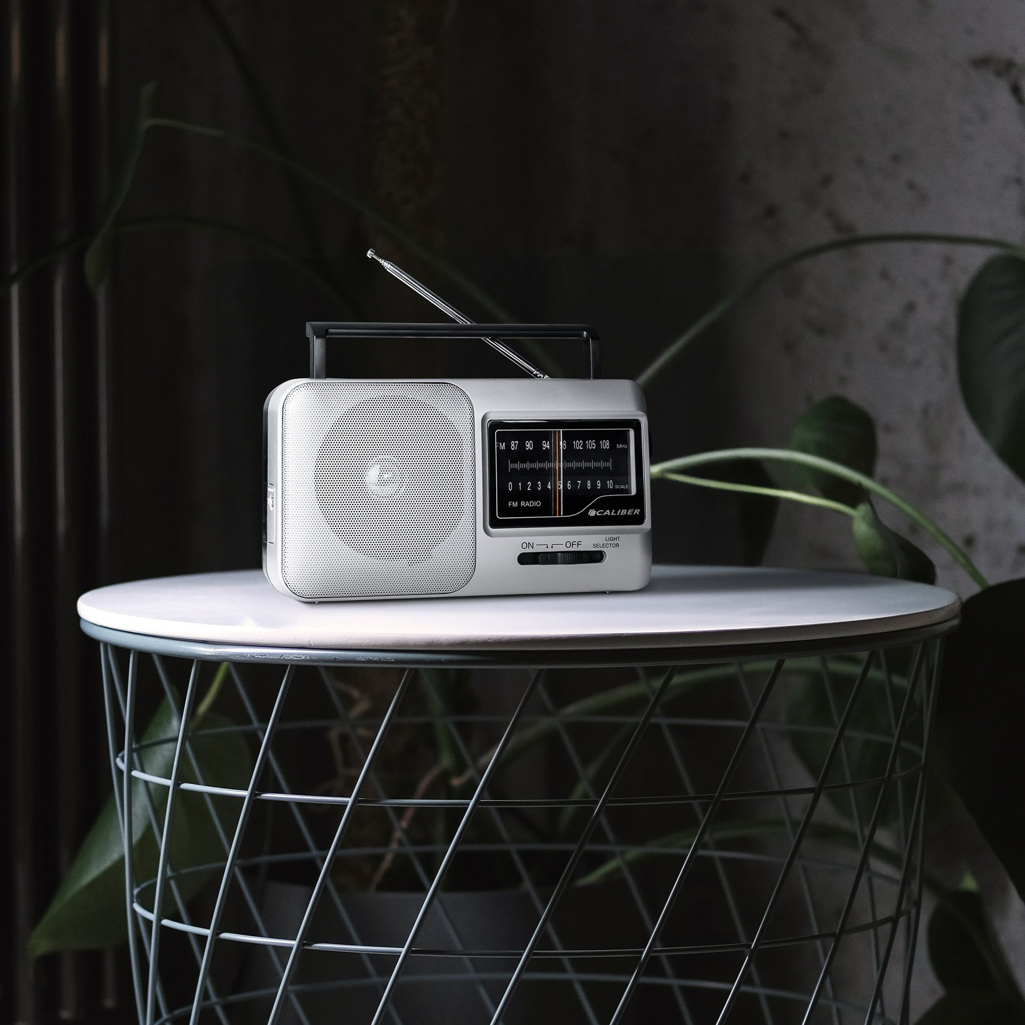 A retro radio on a wire table next to a plant.