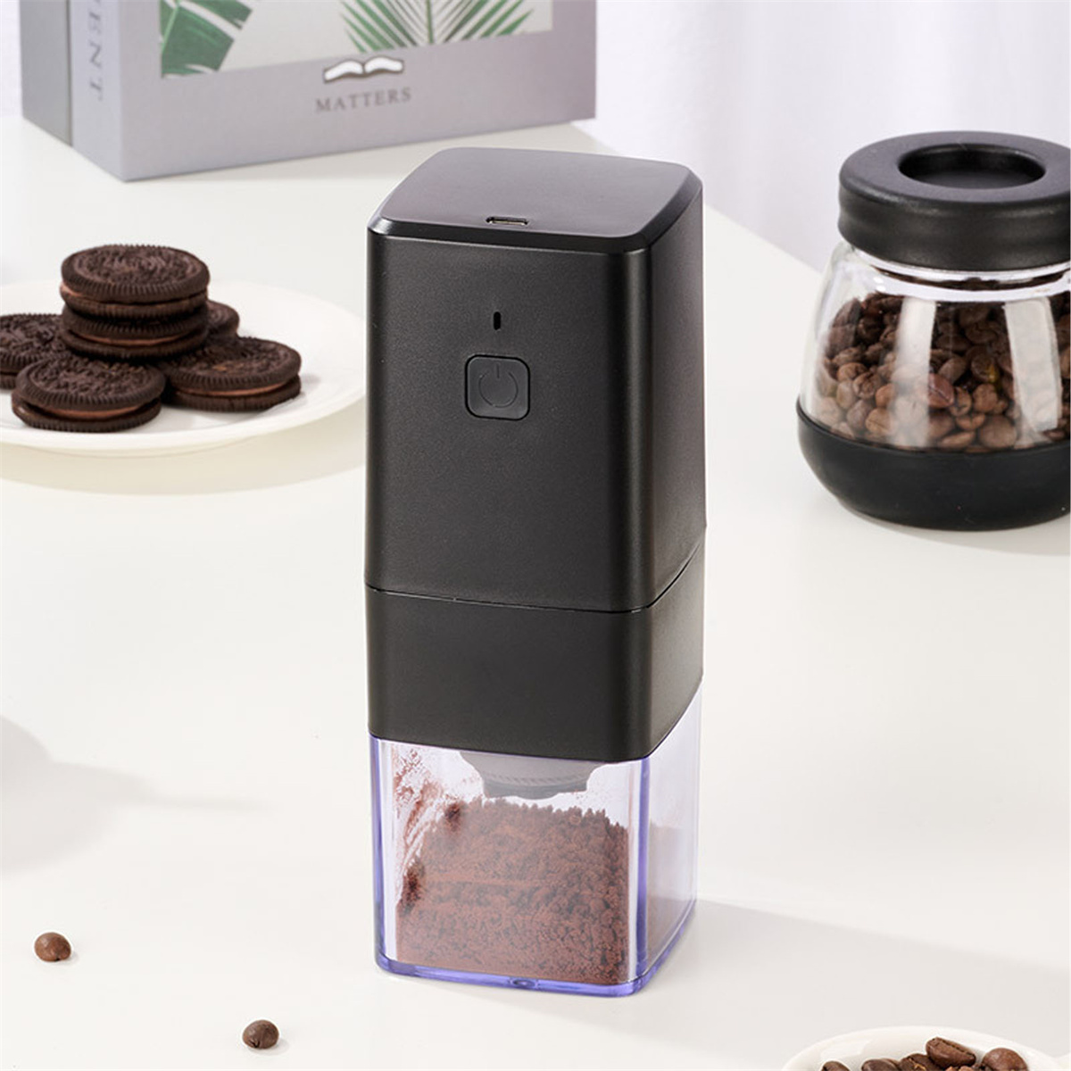 Schwarze Kaffeemühle mit Kaffeepulver im Boden und Keksen.