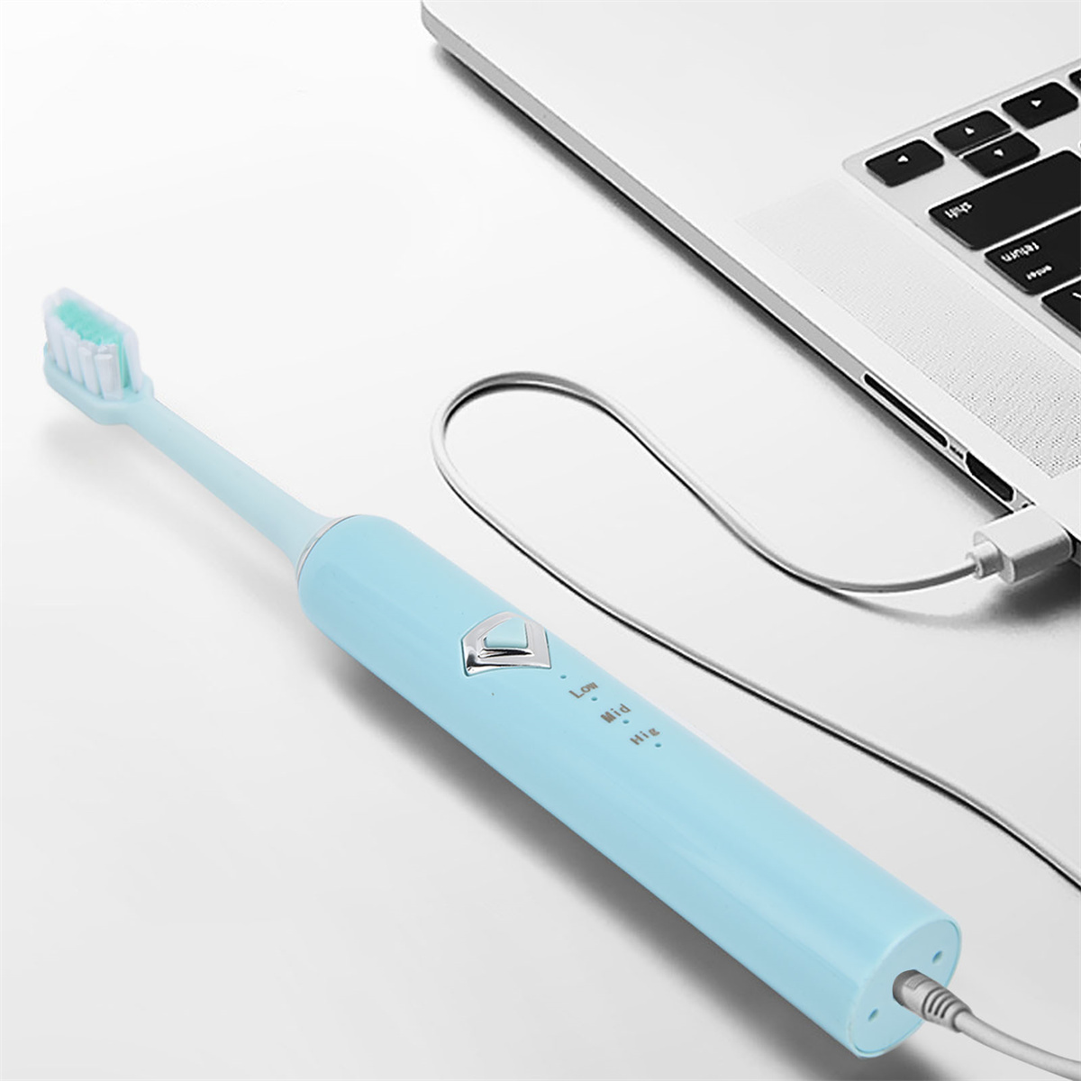 Elektrische blaue Zahnbürste, die von einem Laptop aufgeladen wird. Der Laptop steht auf einer weißen Fläche.