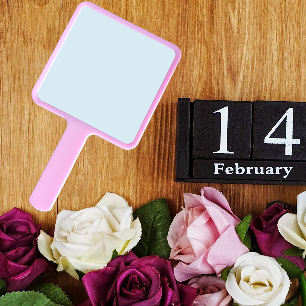 Pinker Handspiegel, Rosen und ein Kalenderblock, der auf den 14. Februar auf Holzgrund steht.
