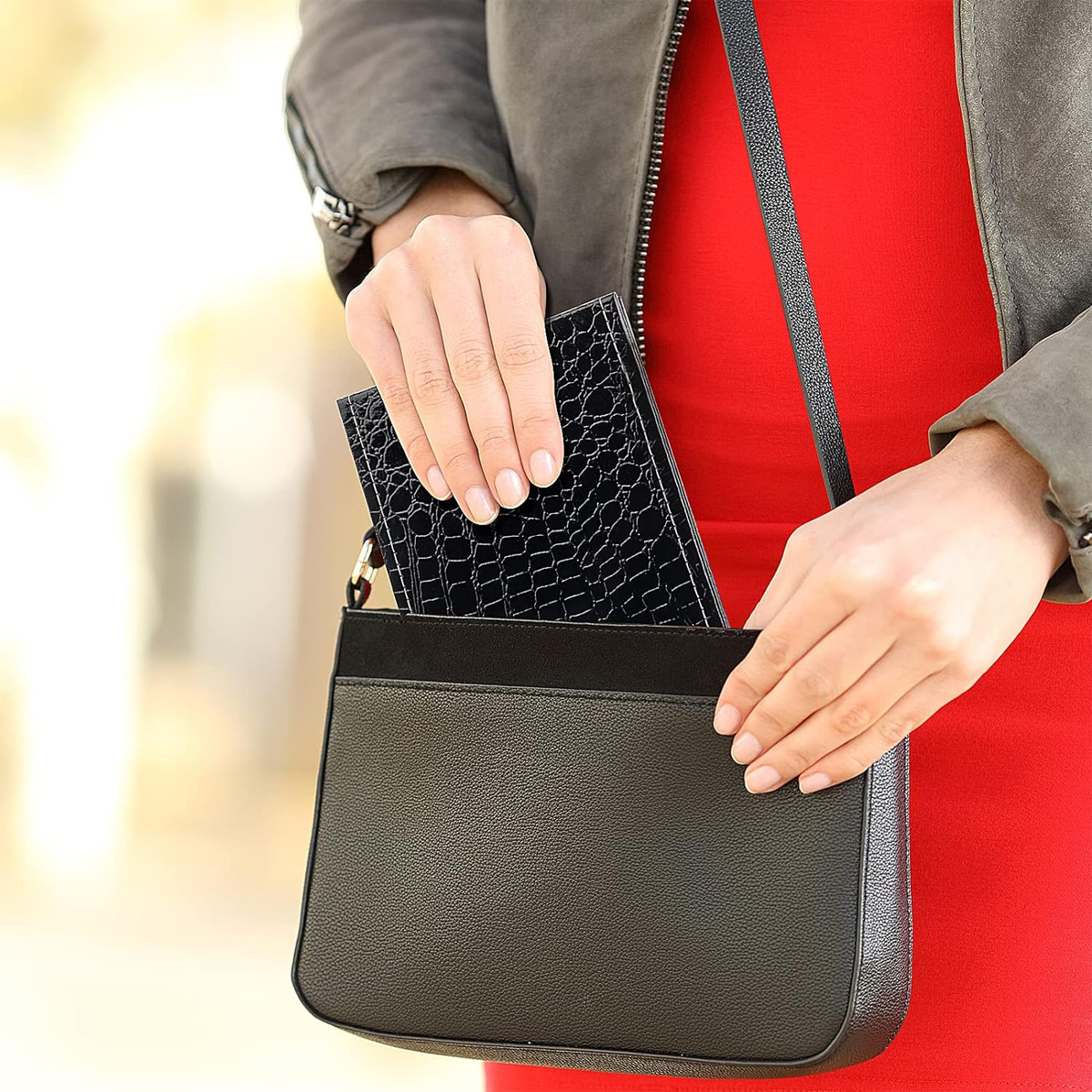 Eine Frau hält eine schwarze Handtasche, legt eine schwarze Geldbörse hinein.
