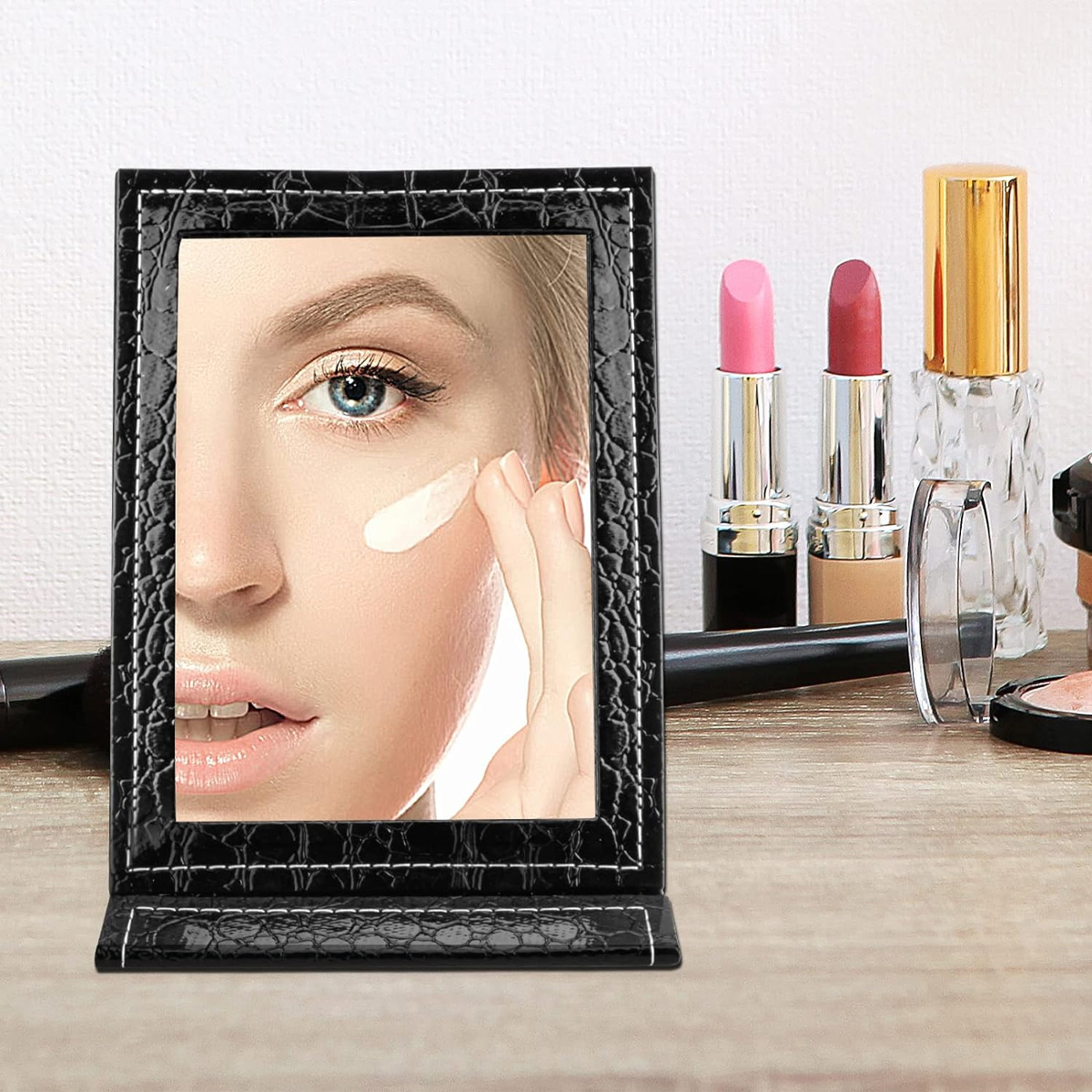 Schminkspiegel. Ein Gesicht im Spiegel, trägt Creme auf. Lippenstift und Parfüm auf dem Tisch.