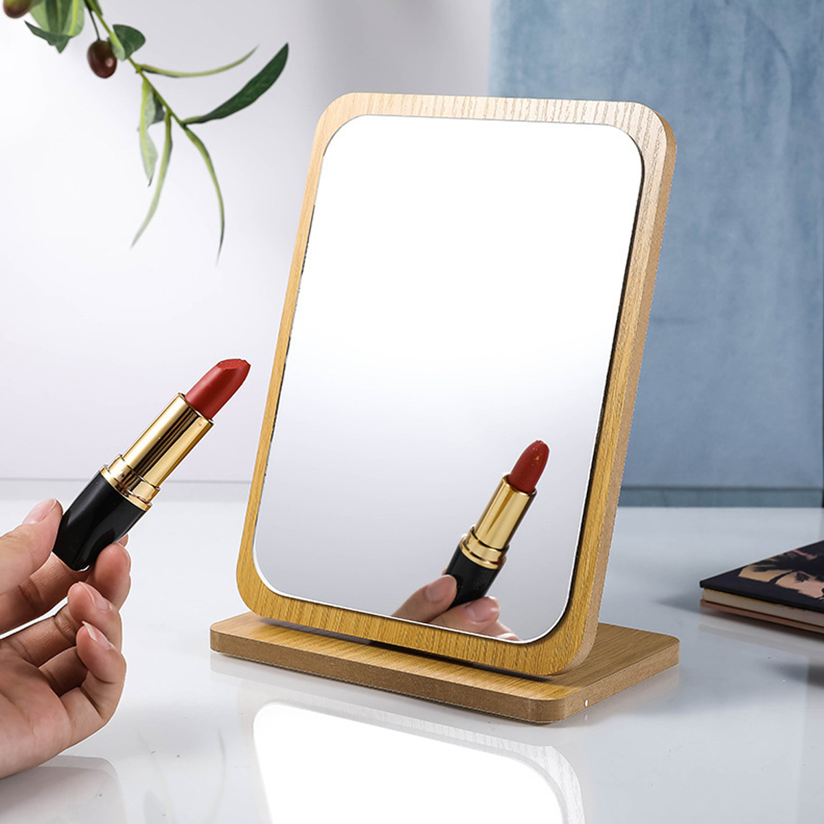 Schminkspiegel mit Lippenstift und Hand. Der Spiegel steht auf weißem Untergrund. Hintergrund blau.