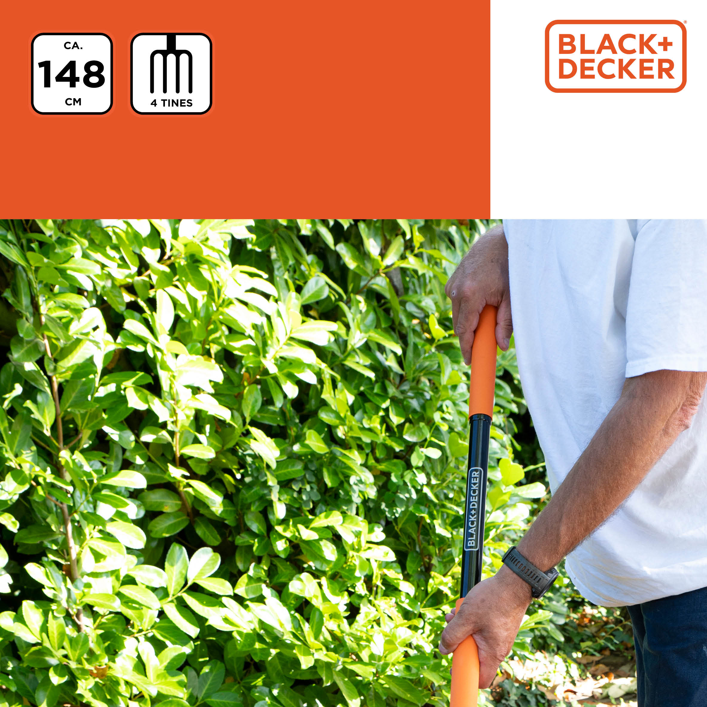 A person holding a garden tool in a garden, orange pole and green bushes, black handle.
