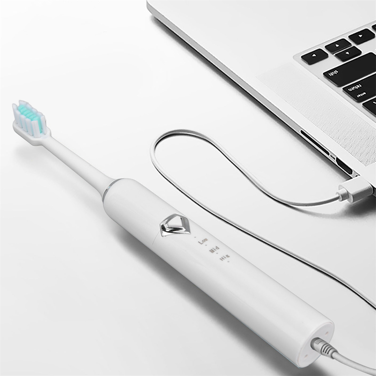 Weiße elektrische Zahnbürste, die neben einem Laptop aufgeladen wird.