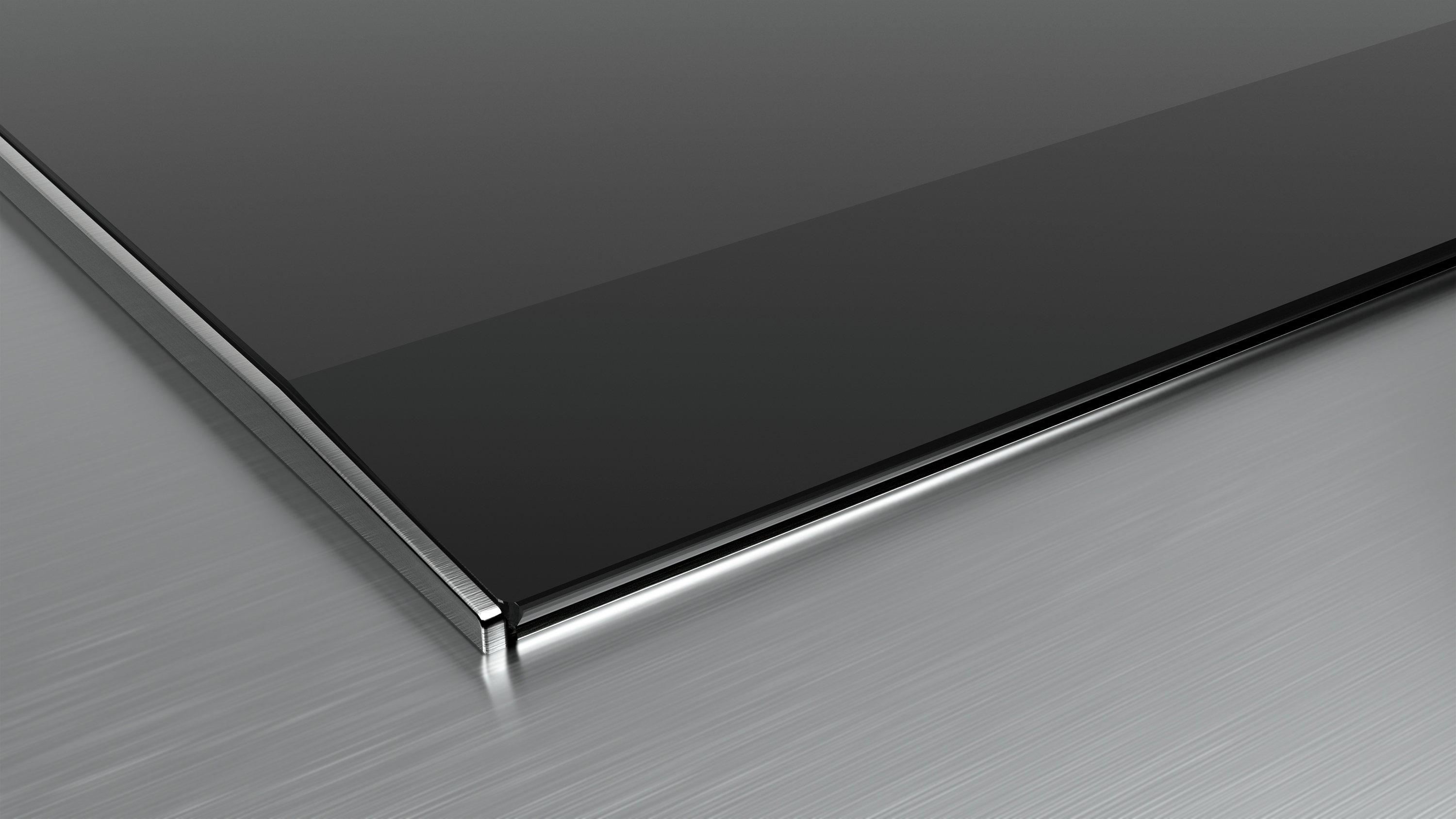 Zbliżenie czarnej szklanej powierzchni ze srebrną krawędzią na szarej, metalicznej powierzchni.