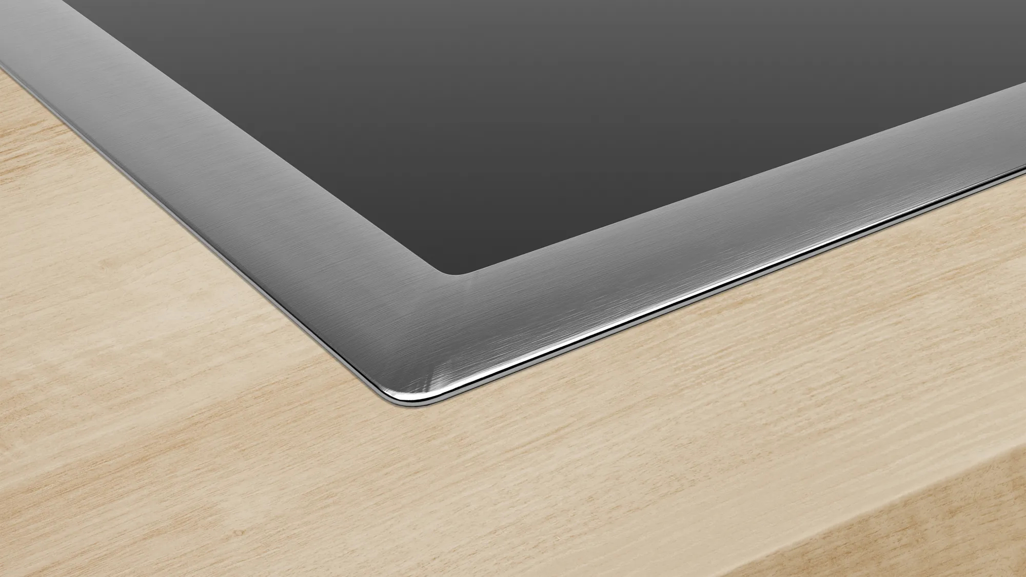 Zbliżenie czarnej płyty grzewczej z ramą ze stali nierdzewnej, na jasnej drewnianej powierzchni.