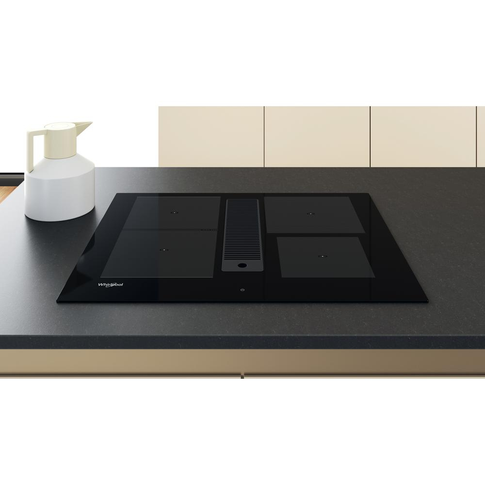 Un piano cottura a induzione nero con quattro fuochi e una brocca bianca su un piano di lavoro.