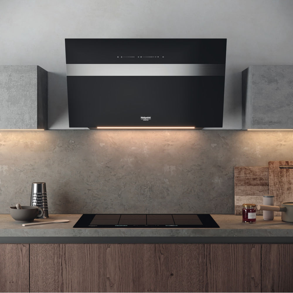 Czarny okap kuchenny nad czarną płytą grzewczą. Wnętrze kuchni z drewnianymi szafkami i blatem.