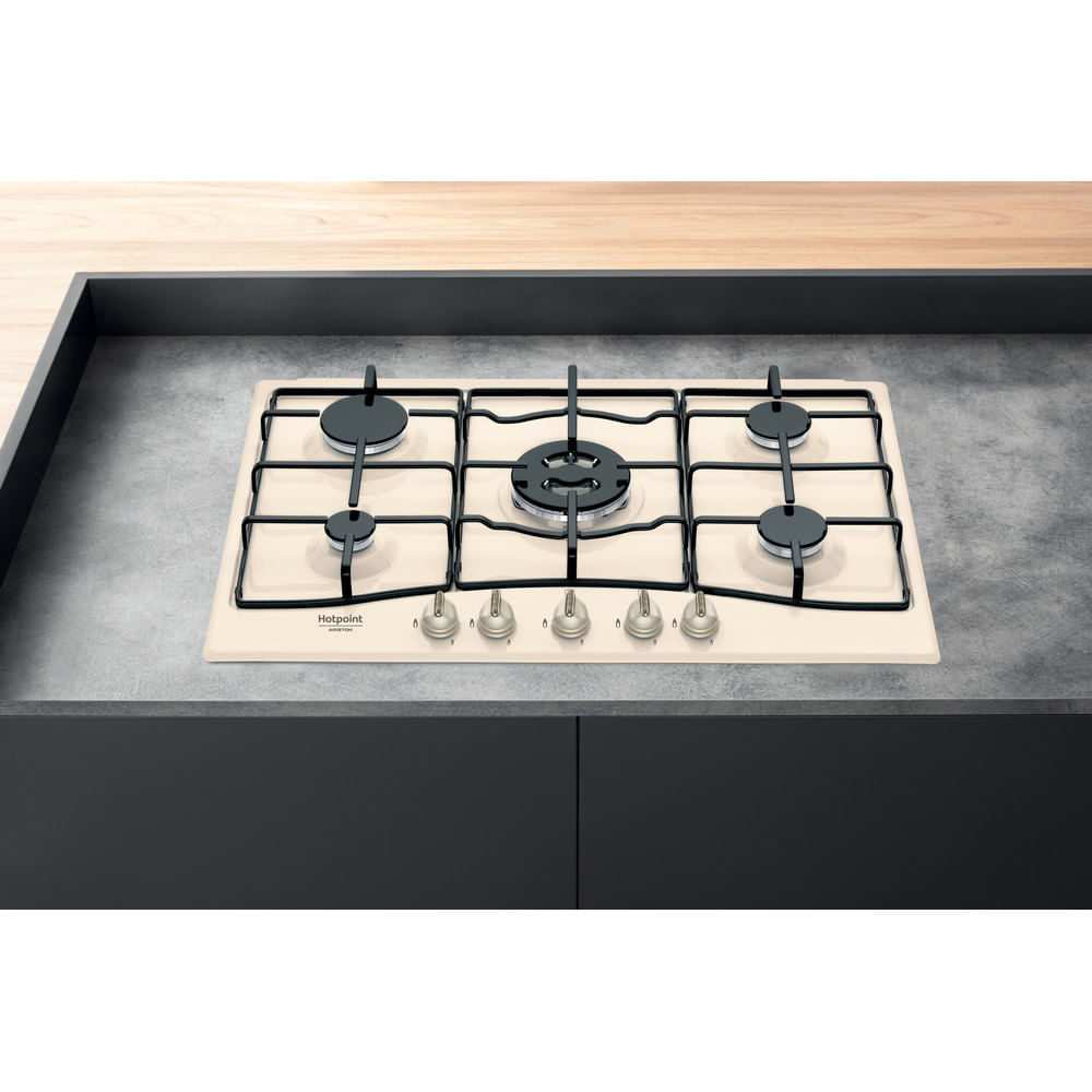 Beżowa płyta gazowa z pięcioma palnikami, czarnymi rusztami i pokrętłami na szarej powierzchni.