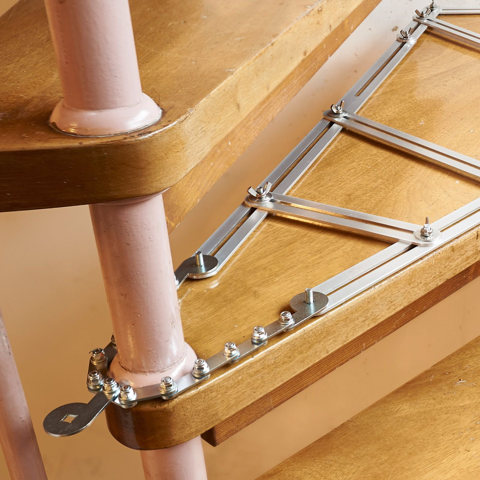Holztreppe mit Metallstützen. Die Stütze hat rosa Farbe mit Schrauben und einem schlüsselförmigen Mechanismus.