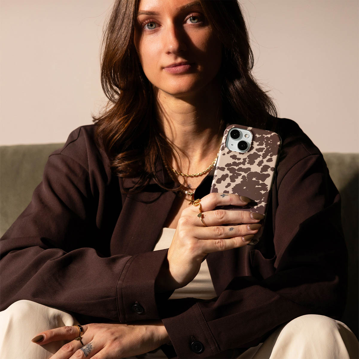 Vrouw die een telefoon met koeienprint hoesje vasthoudt, bruine blazer.