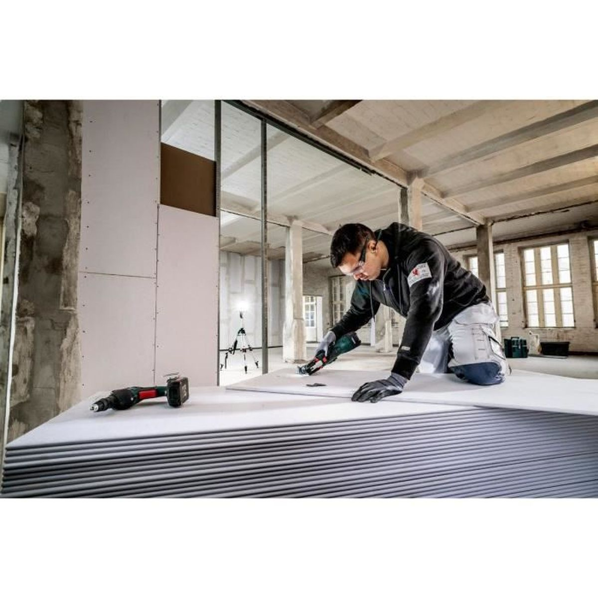 Mężczyzna tnie płyty gipsowo-kartonowe. Używa narzędzia do cięcia płyt gipsowo-kartonowych. Pomieszczenie jest w budowie.