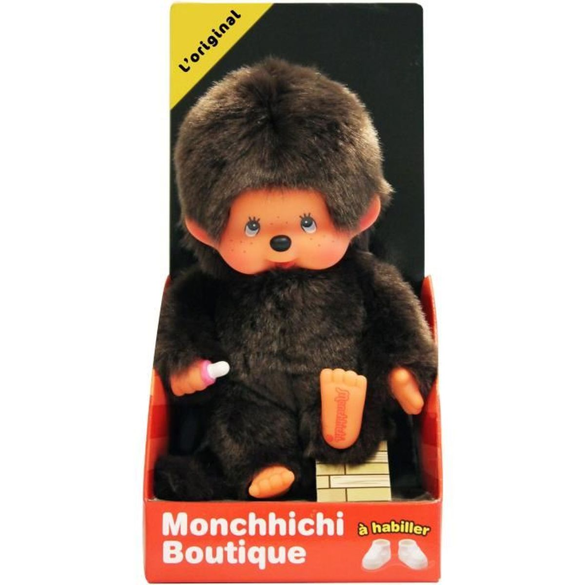 Lalka Monchhichi w pudełku. Lalka jest brązowa z futrzaną głową i trzyma butelkę.
