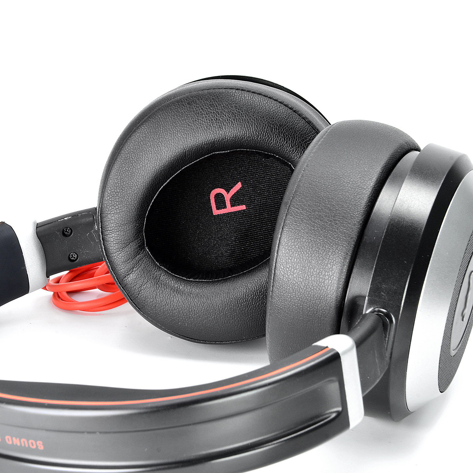 Casque noir avec des accents rouges sur une surface blanche. La lettre 'R' est visible sur l'écouteur.