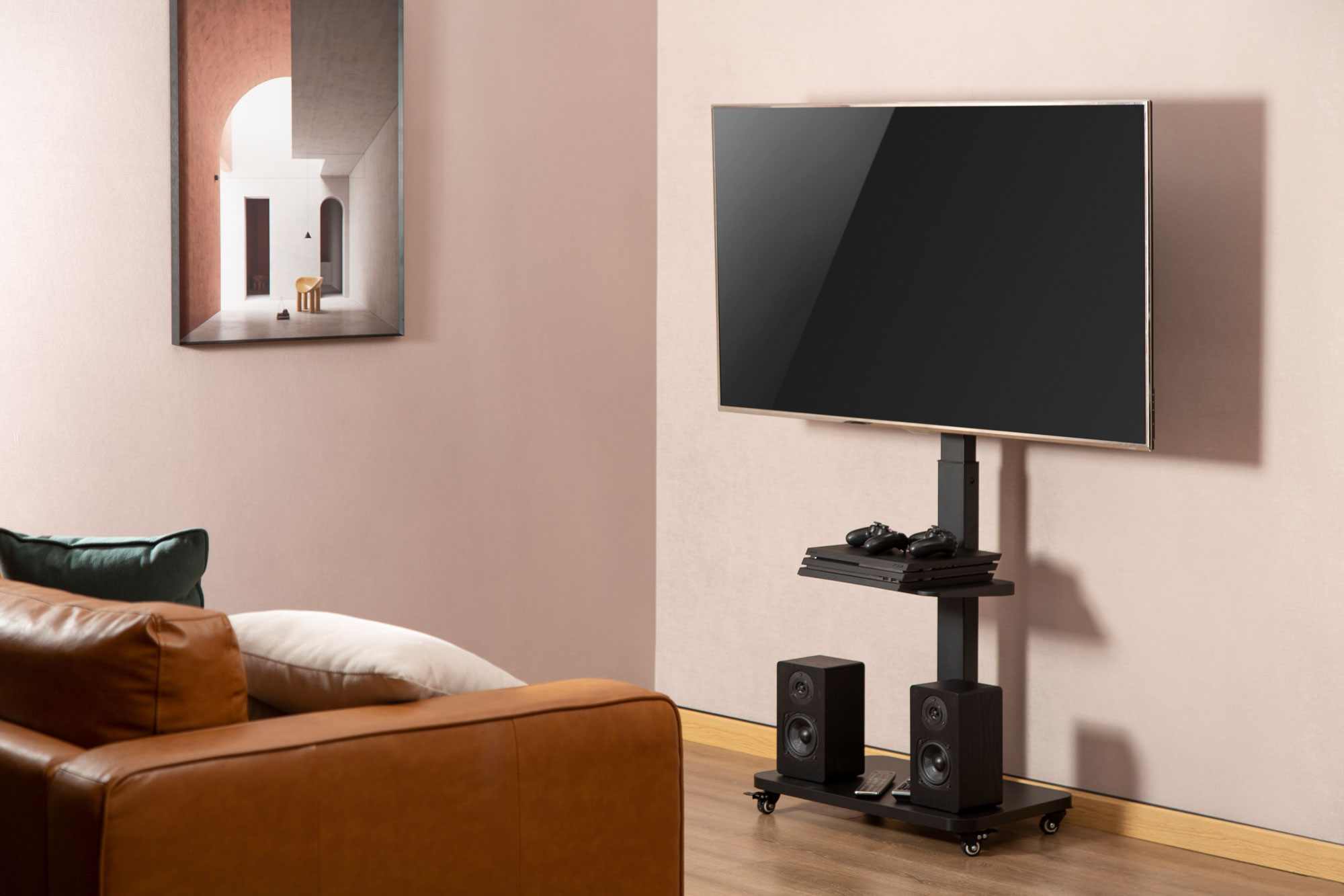 Wohnzimmer mit Fernseher auf einem schwarzen Rollständer, Lautsprechern und einem braunen Ledersofa.