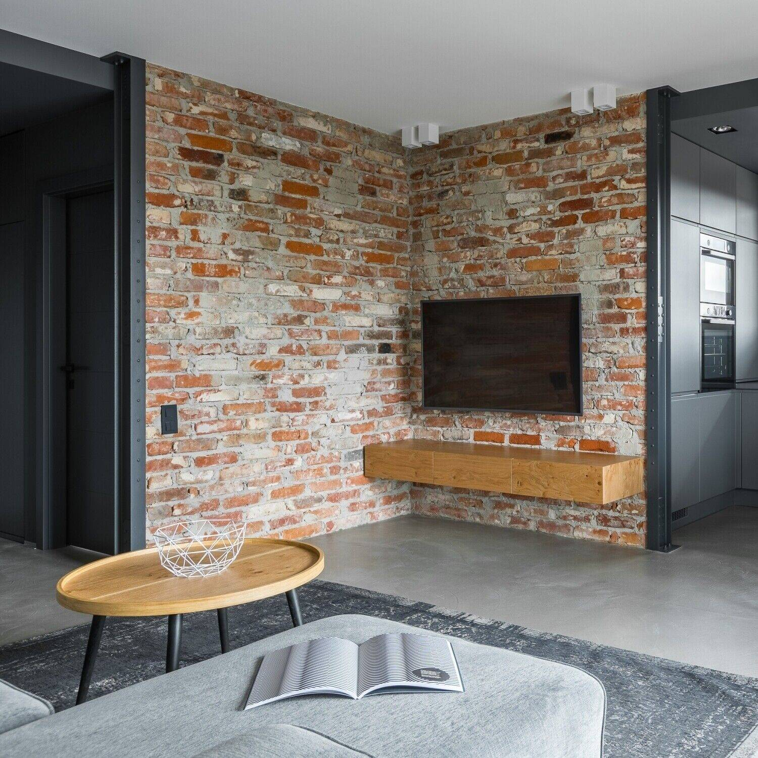 Wohnzimmer mit Backsteinmauer, TV, Couch, Couchtisch, Teppich und offenem Buch, modernes Interieur.