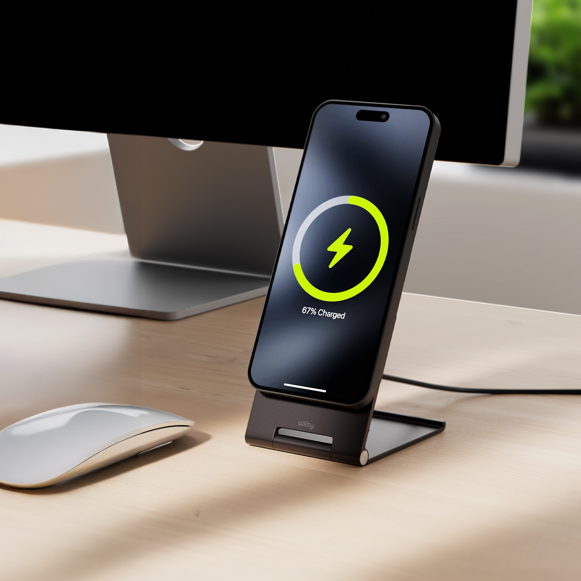 Telefon ładujący się na stojaku, pokazujący symbol ładowania. Widoczna mysz i monitor.
