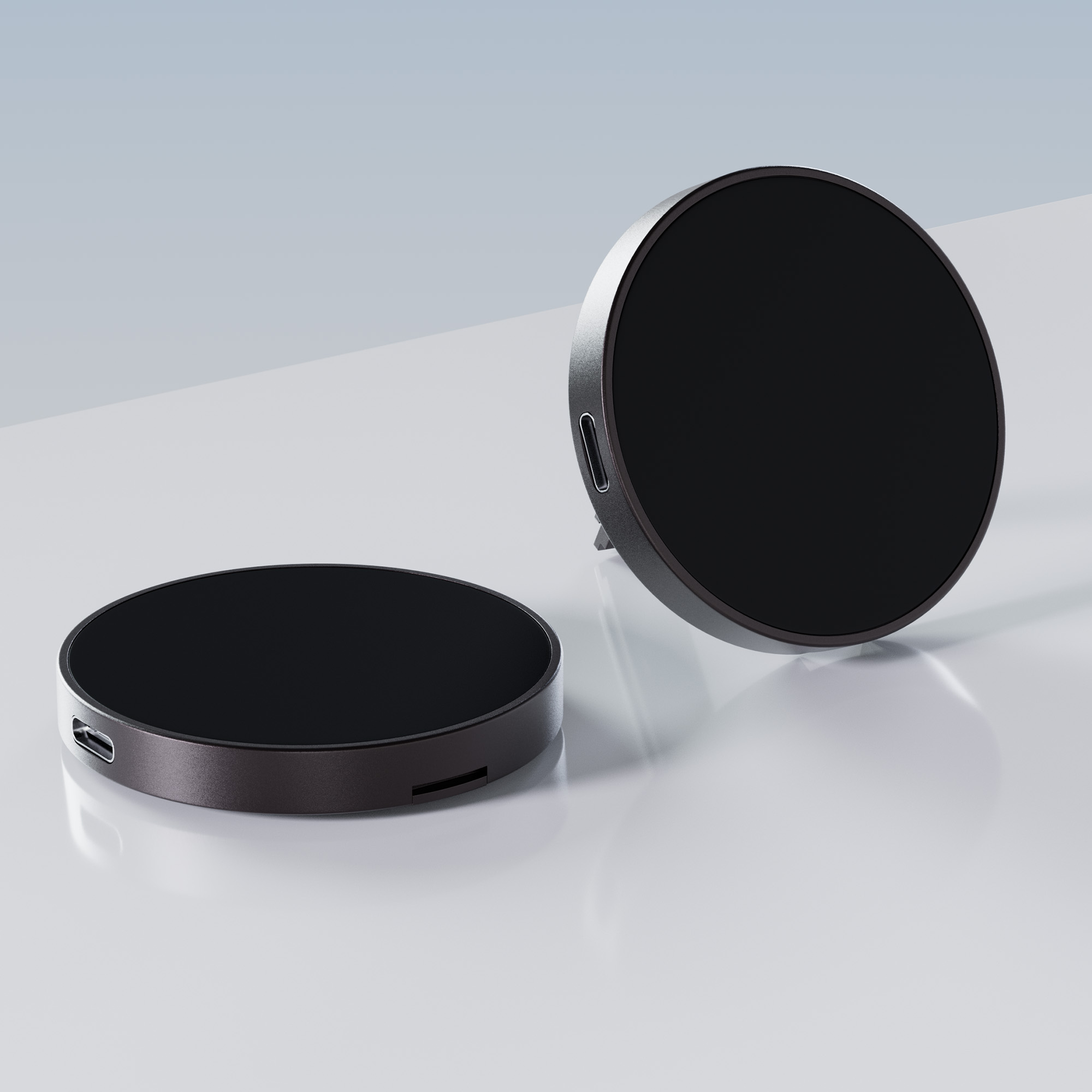 Dwie czarne bezprzewodowe podkładki ładujące, okrągły kształt, szare tło, widok z boku.