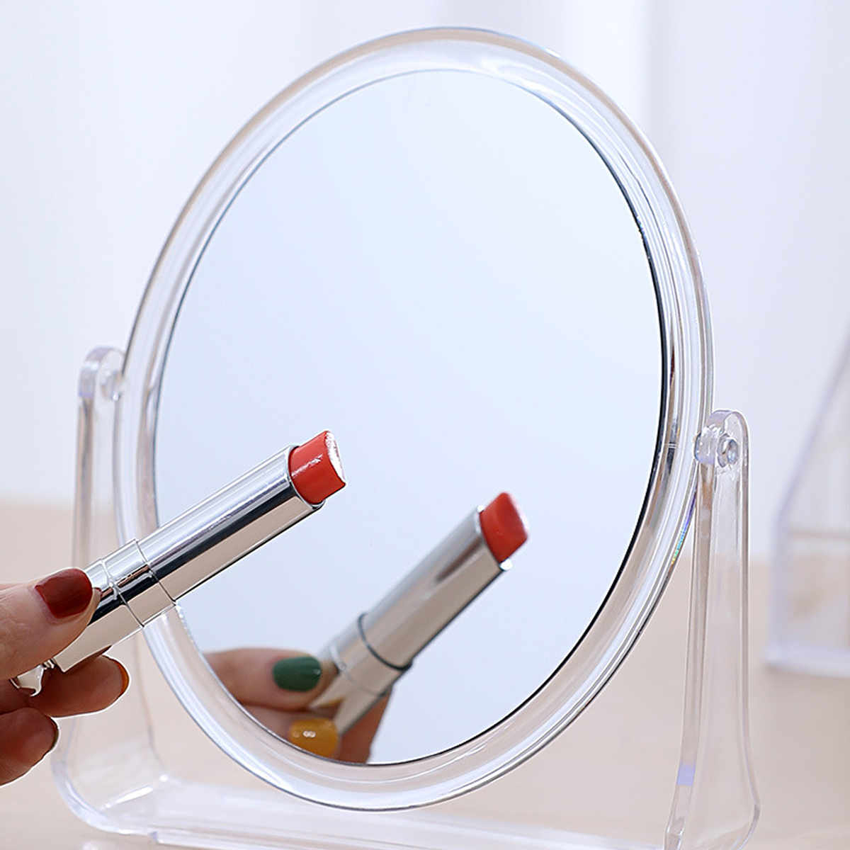Spiegel mit einer Hand, die einen Lippenstift hält. Spiegelbild des Lippenstifts und der Hand.