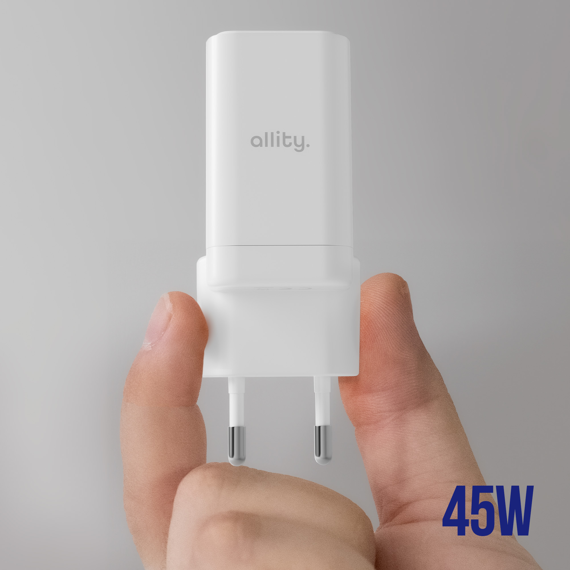 Biała ładowarka trzymana w dłoni. Biała obudowa, srebrne piny, 'allity.' i 45W.