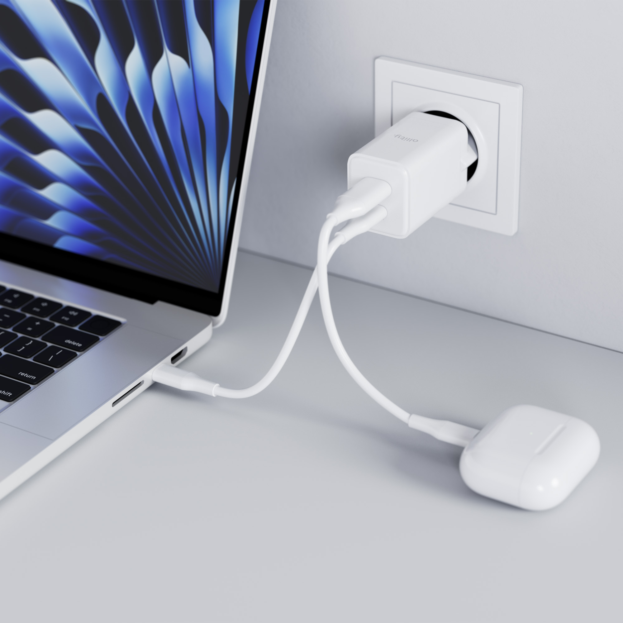 Biała ładowarka w gniazdku. Laptop i etui AirPods połączone kablami.