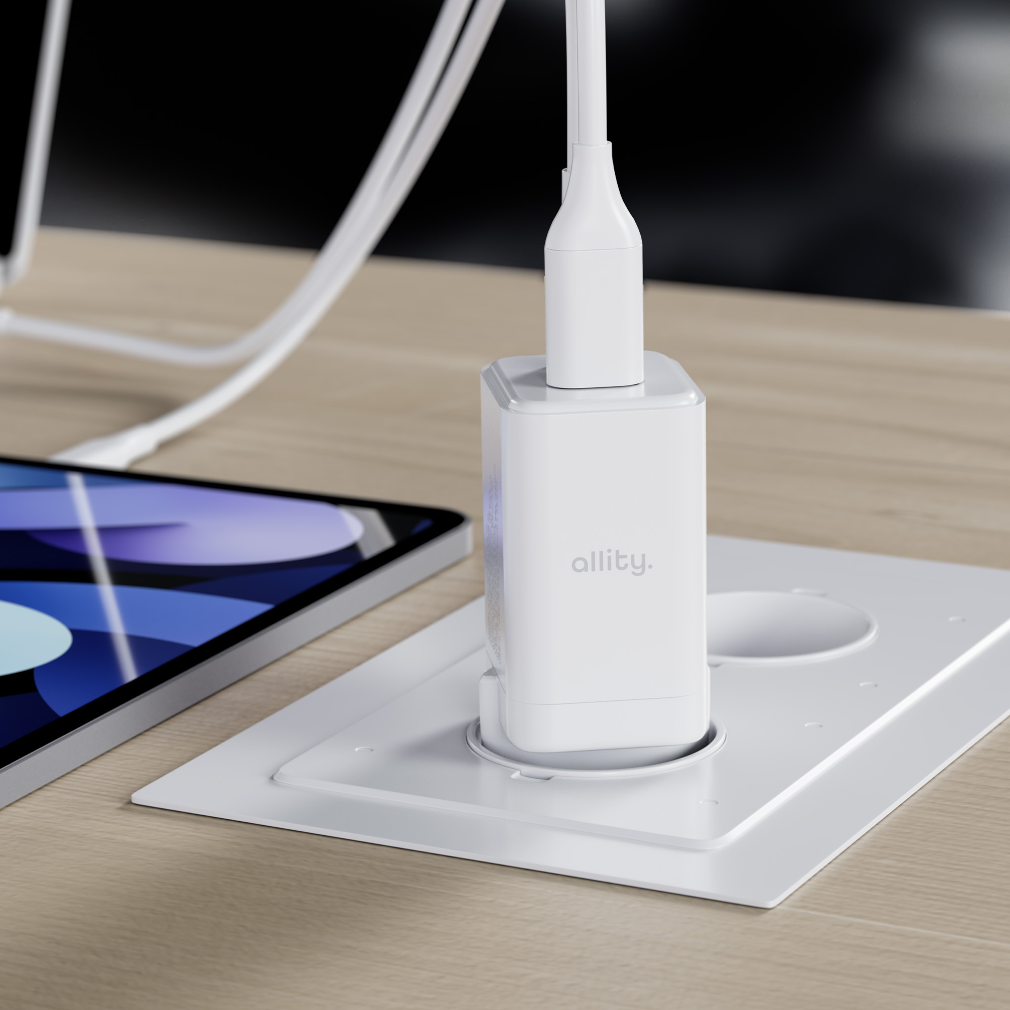 Biała ładowarka wpięta w białą podstawę na drewnianym stole. Po lewej tablet.