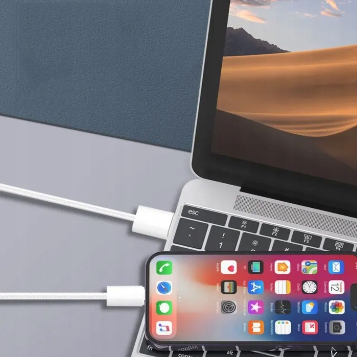 Laptop podłączony do smartfona za pomocą białego kabla. Telefon wyświetla ekran aplikacji.