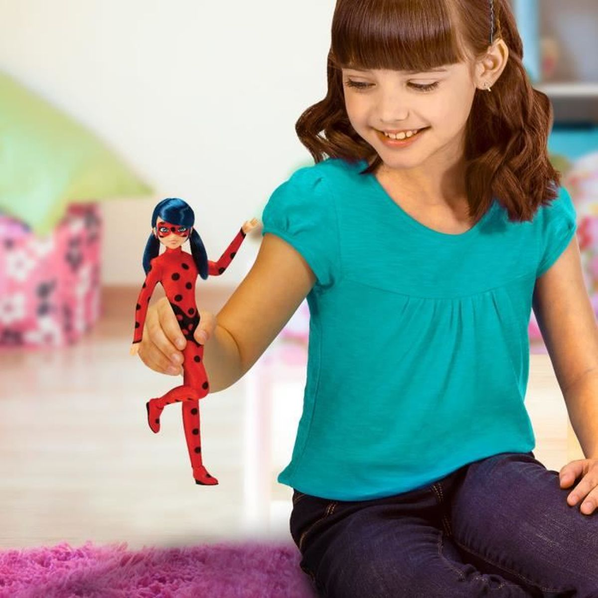 Ein Mädchen hält eine Puppe, die einer Superheldin ähnelt, in einem Raum mit unscharfem Hintergrund.