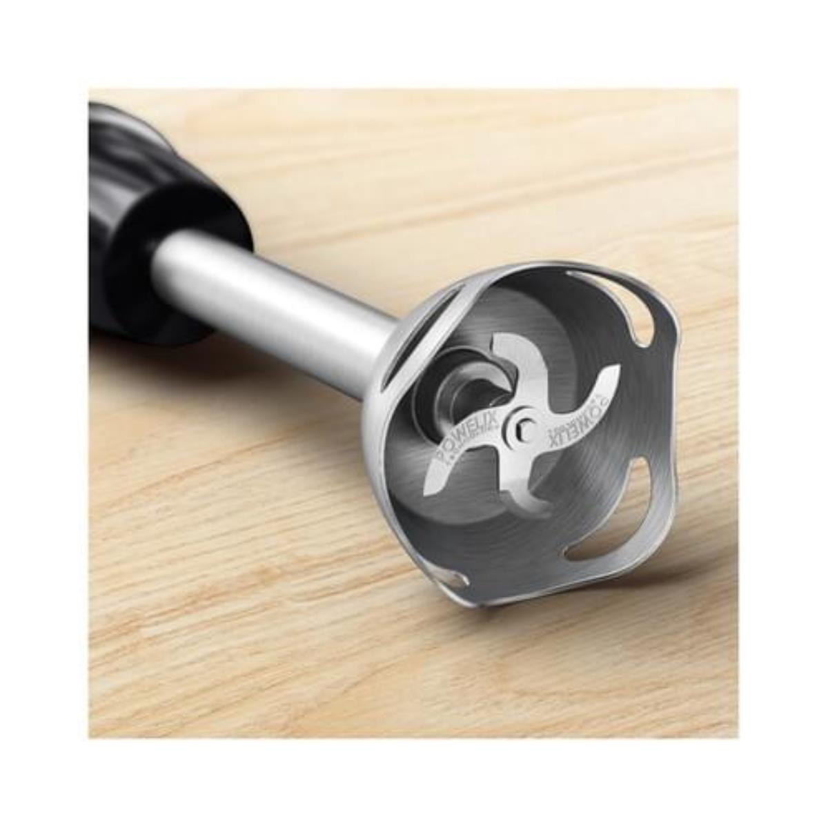 Een metalen blenderkop met messen, op een houten oppervlak. De merknaam is zichtbaar.