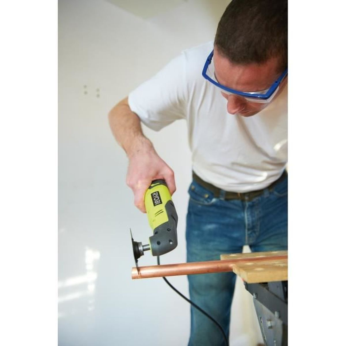 Mann benutzt ein oszillierendes Handwerkzeug, um ein Kupferrohr zu schneiden. Schutzbrille wird getragen.