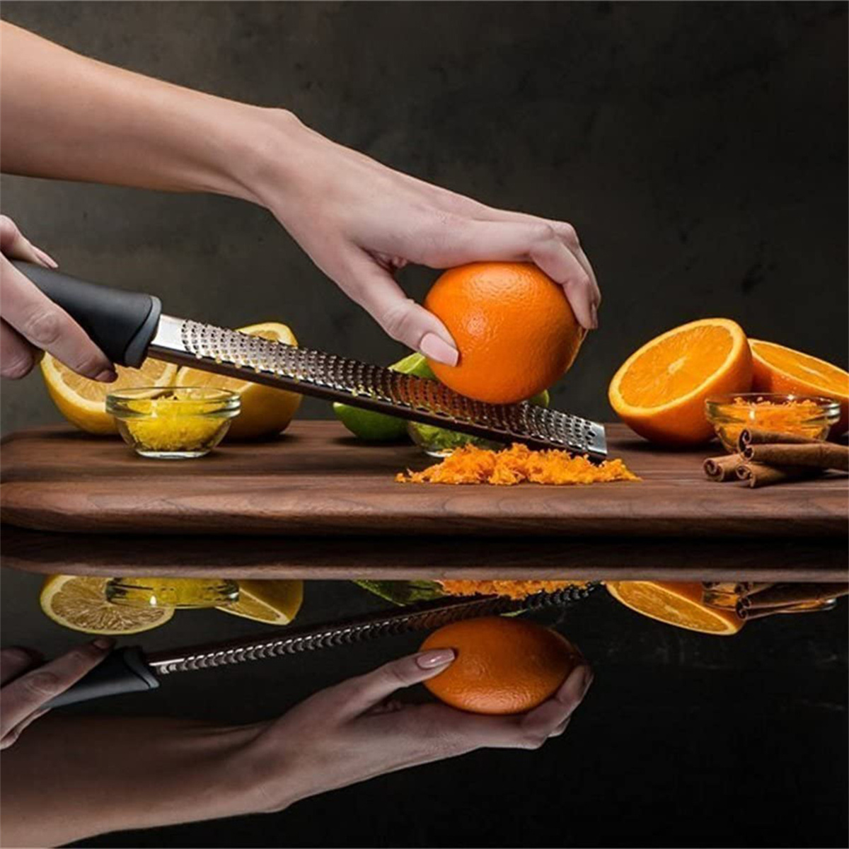 Hände, die eine Orange über einem Holzbrett abreiben. Zitrone, Limette und Zimtstangen.