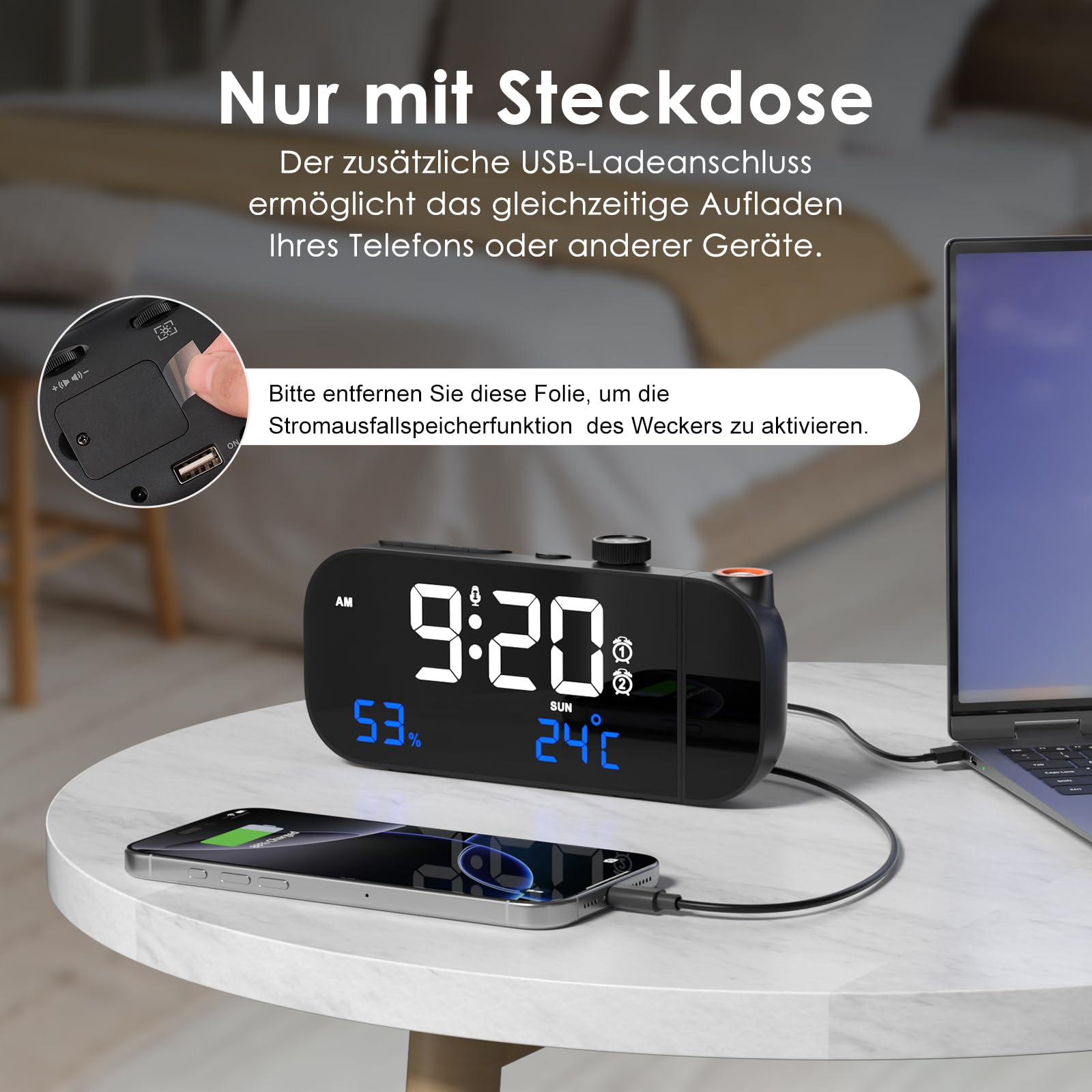 Schwarzer Wecker mit Digitalanzeige. Telefon wird auf dem Tisch geladen. Tisch und Laptop sichtbar.