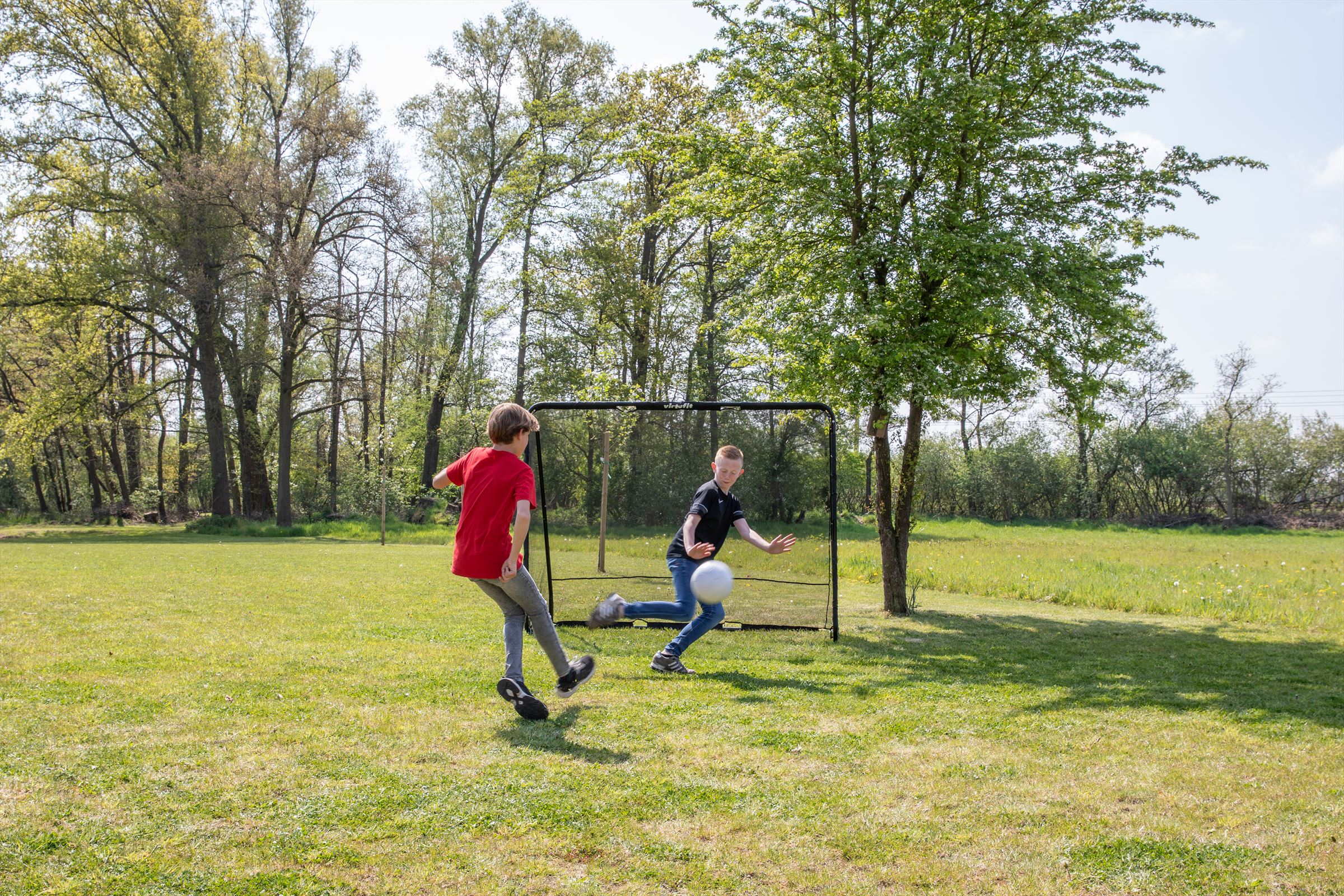 Due ragazzi giocano a calcio su un campo erboso, uno calcia la palla verso la porta.